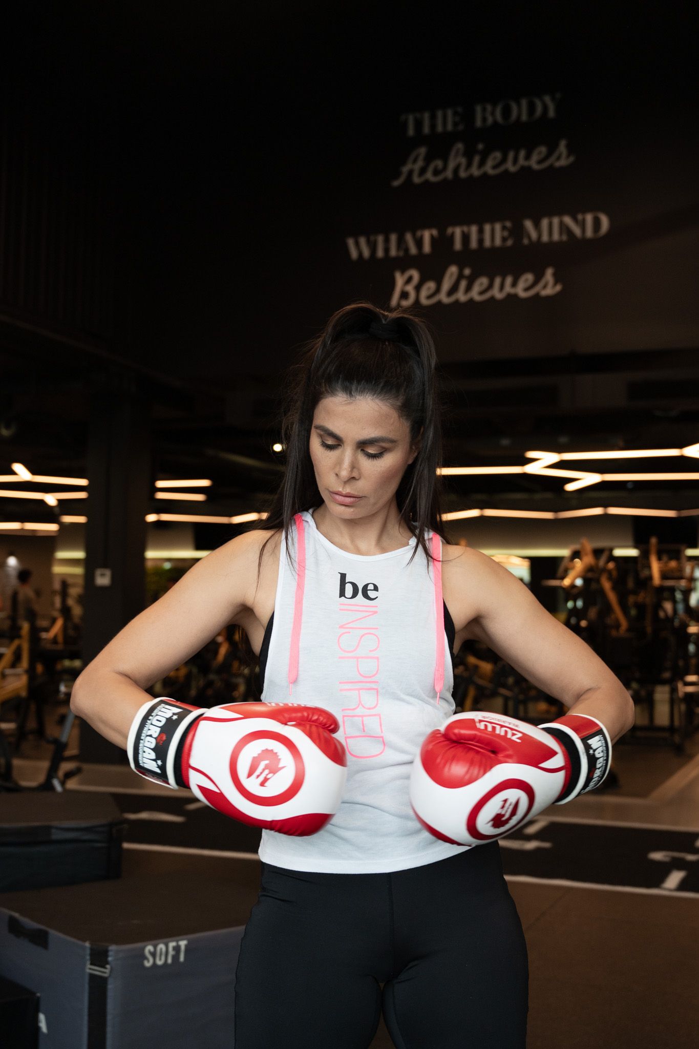 Athletic woman in boxing gloves at a gym with motivational quote on the wall behind her.