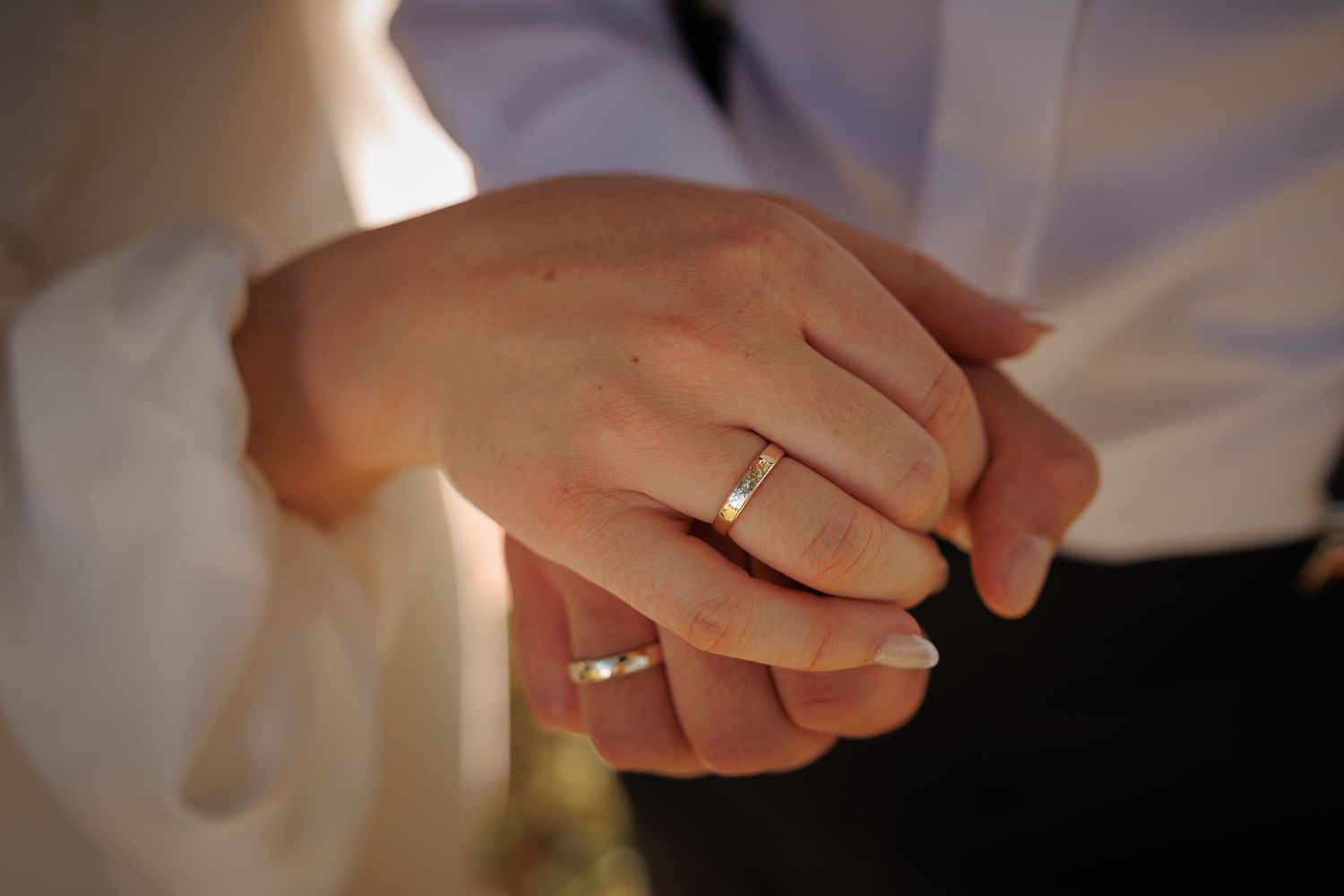 Close-up shot of wedding rings and clasped hands showing newly married couple's commitment.