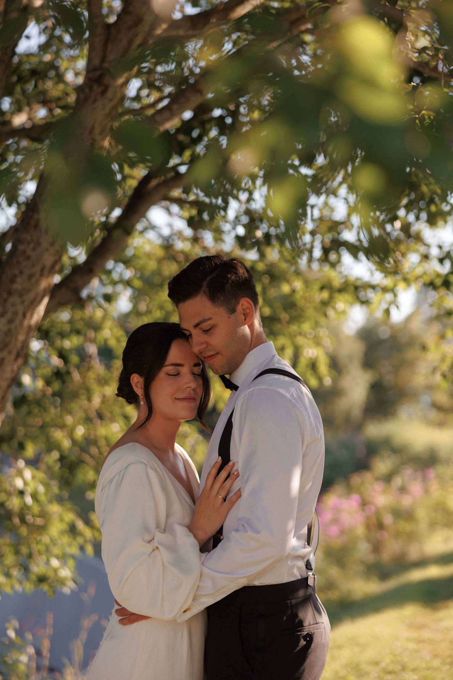 Intimate moment between newlyweds in soft golden sunlight filtered through tree leaves.