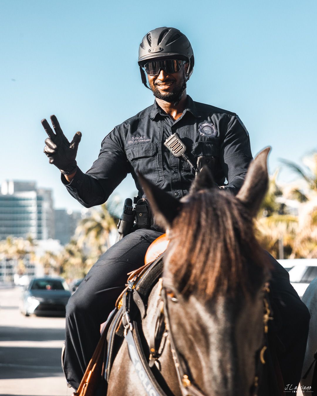 Mounted police officer in uniform making peace sign while patrolling city street.
