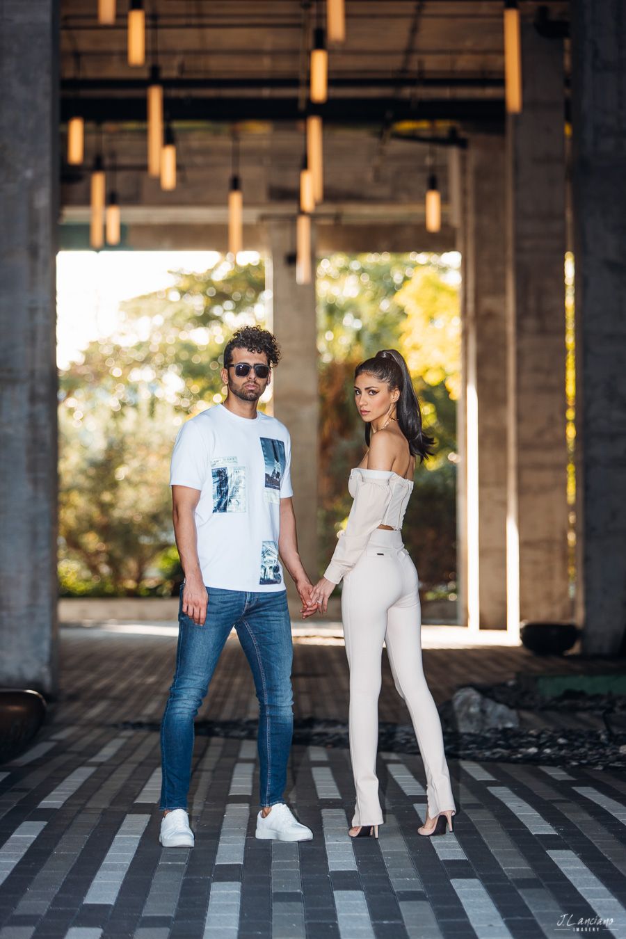 Stylish couple poses under modern architectural structure with hanging lights.