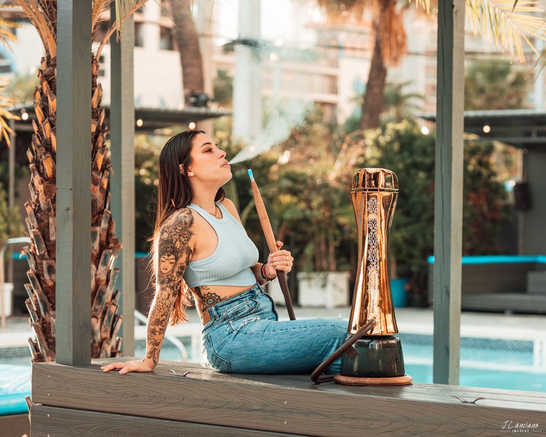 Woman relaxing by pool with hookah and champagne bottle at luxury resort.