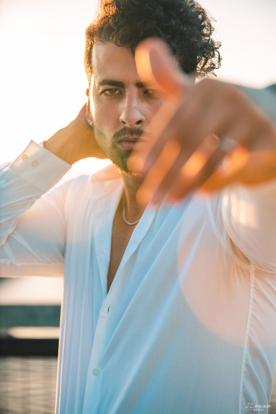 Fashion portrait of man in white shirt with hand raised during golden hour.