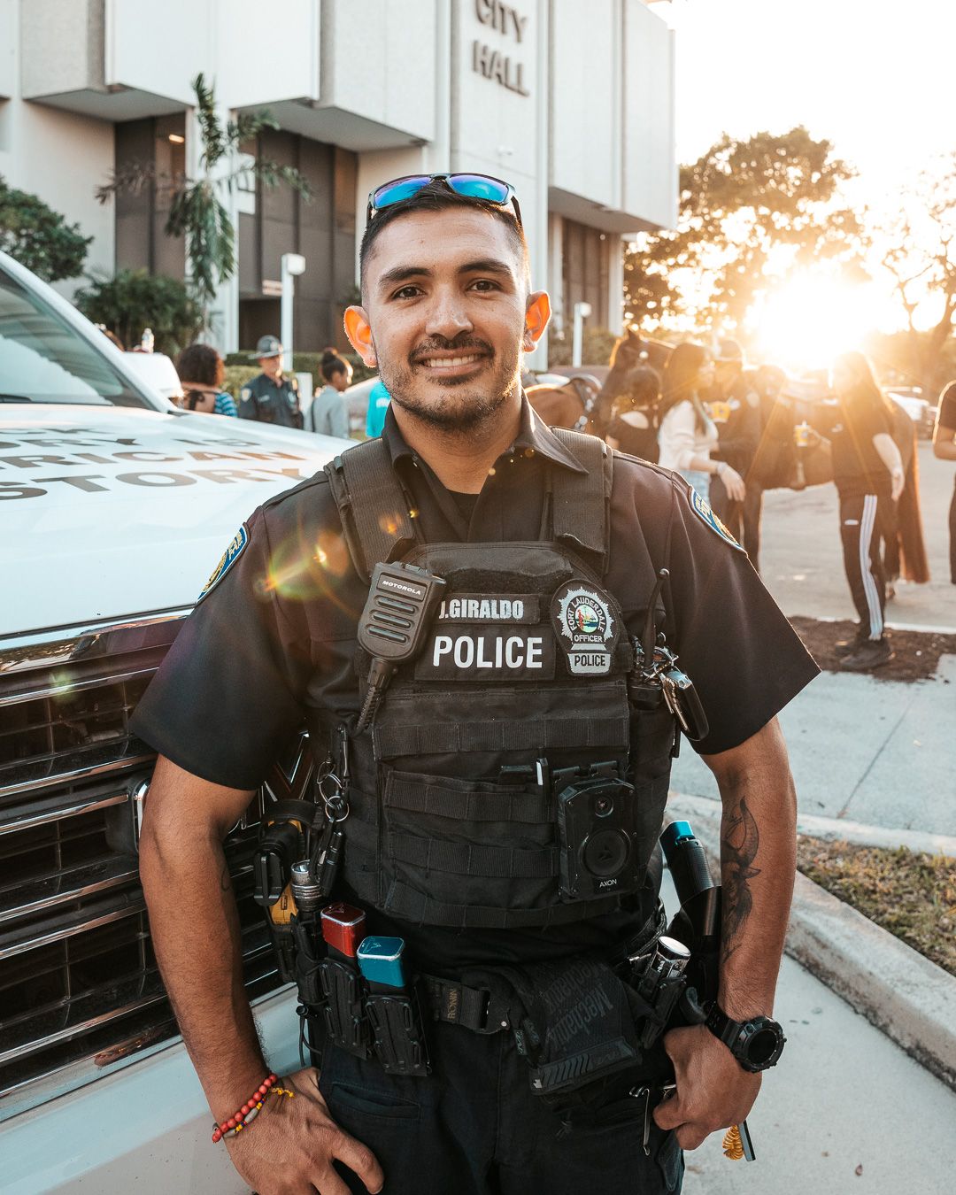 Police officer in tactical vest poses in front of city hall during golden hour sunset.