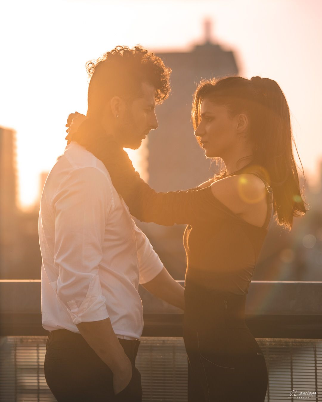 Romantic couple embracing during sunset with city backdrop.