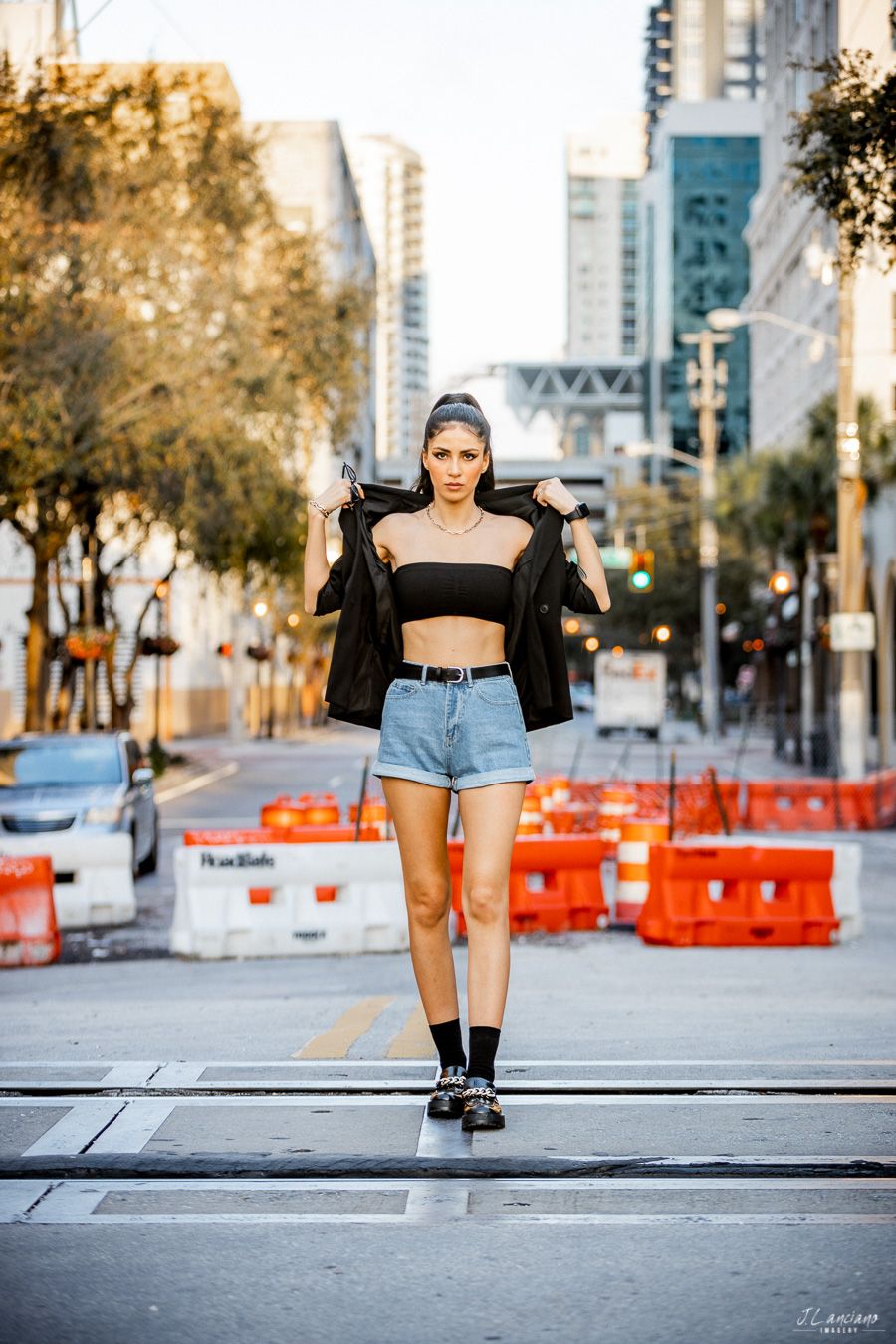 Urban fashion portrait of woman in black crop top and denim shorts on city street.