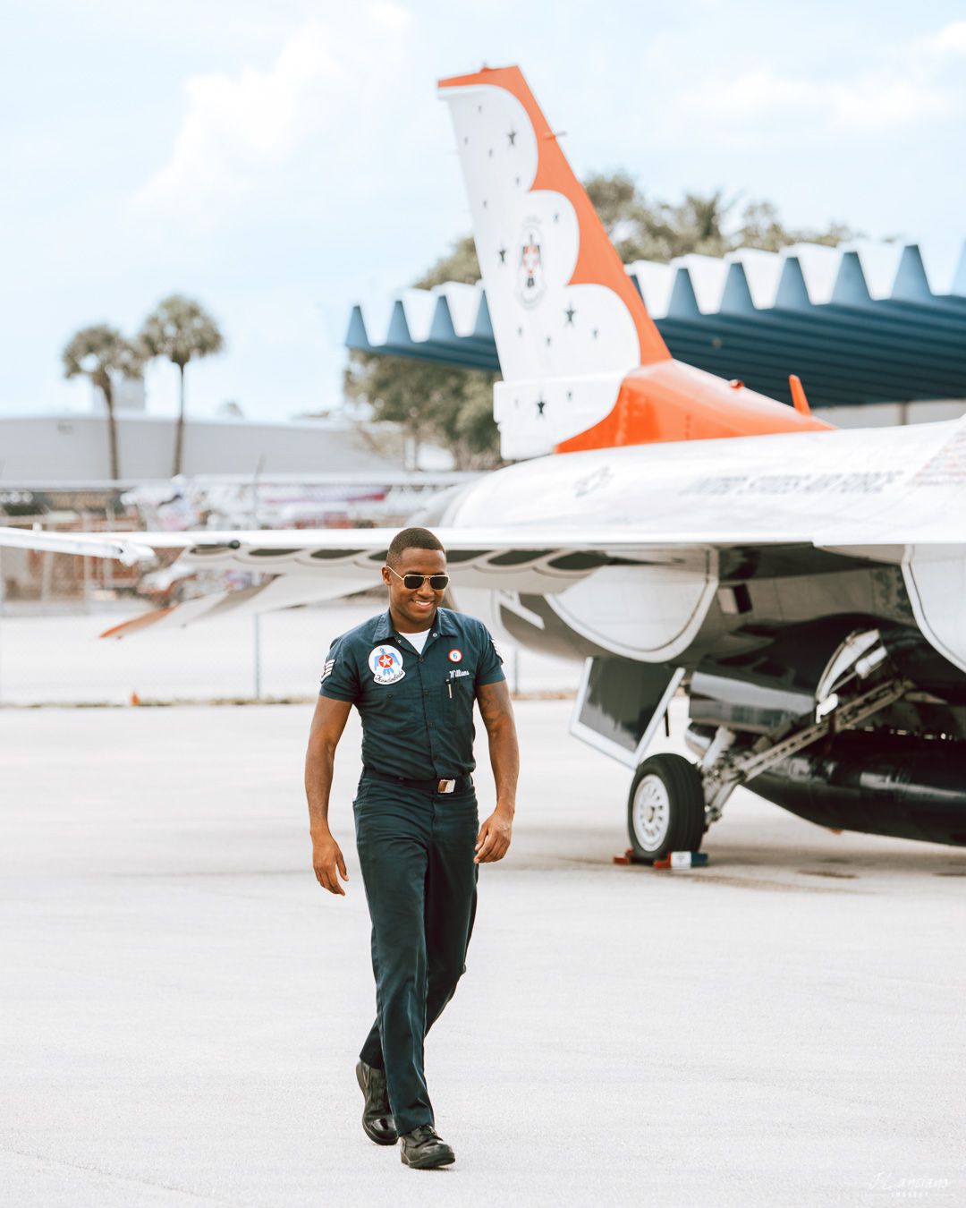 Uniformed officer walks confidently past small aircraft on sunny tarmac.