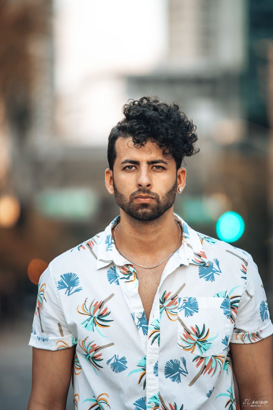 A person wearing a tropical print short-sleeve shirt poses against an urban background with bokeh lights.