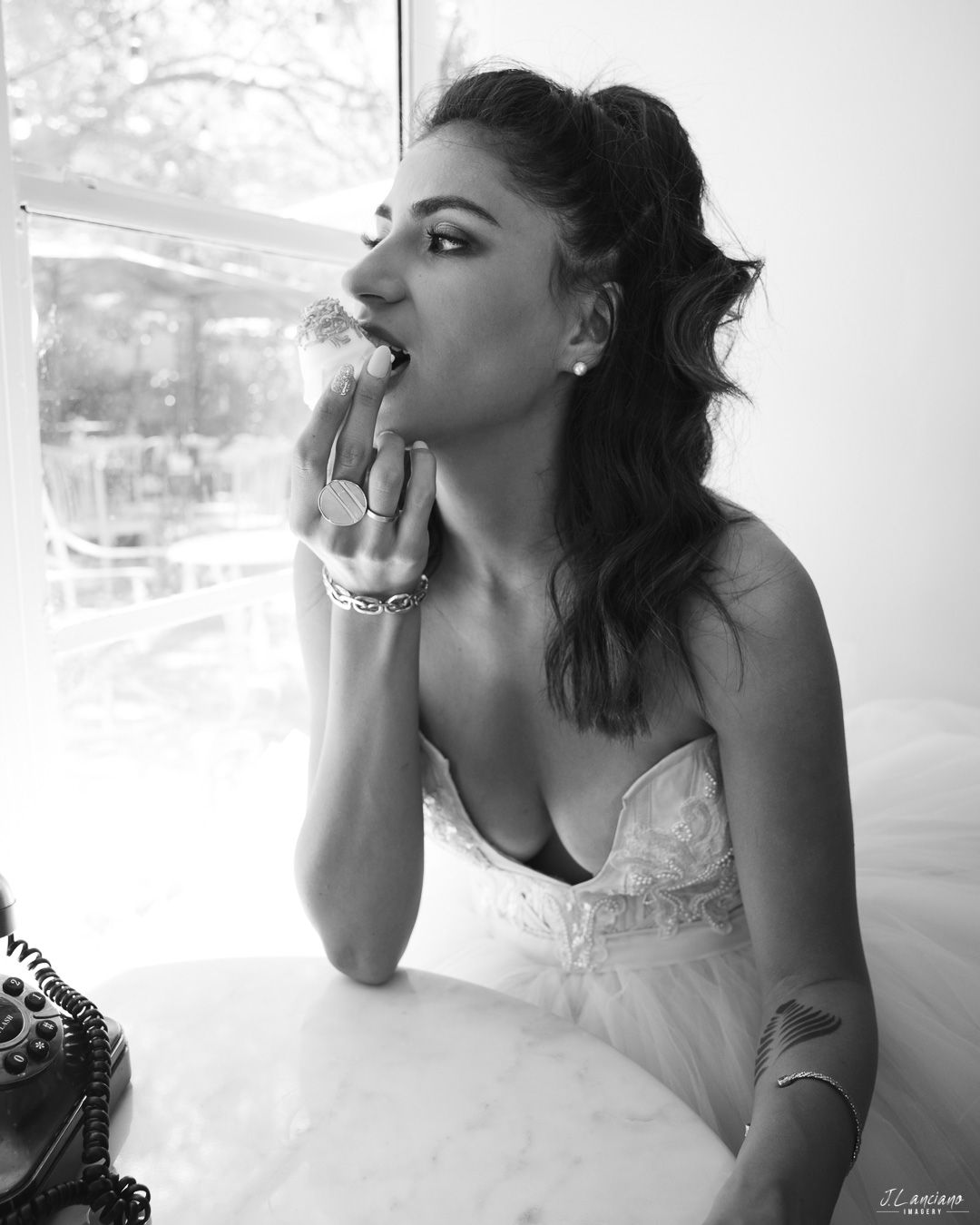 A black and white portrait of a person in a wedding dress posing thoughtfully by a window.
