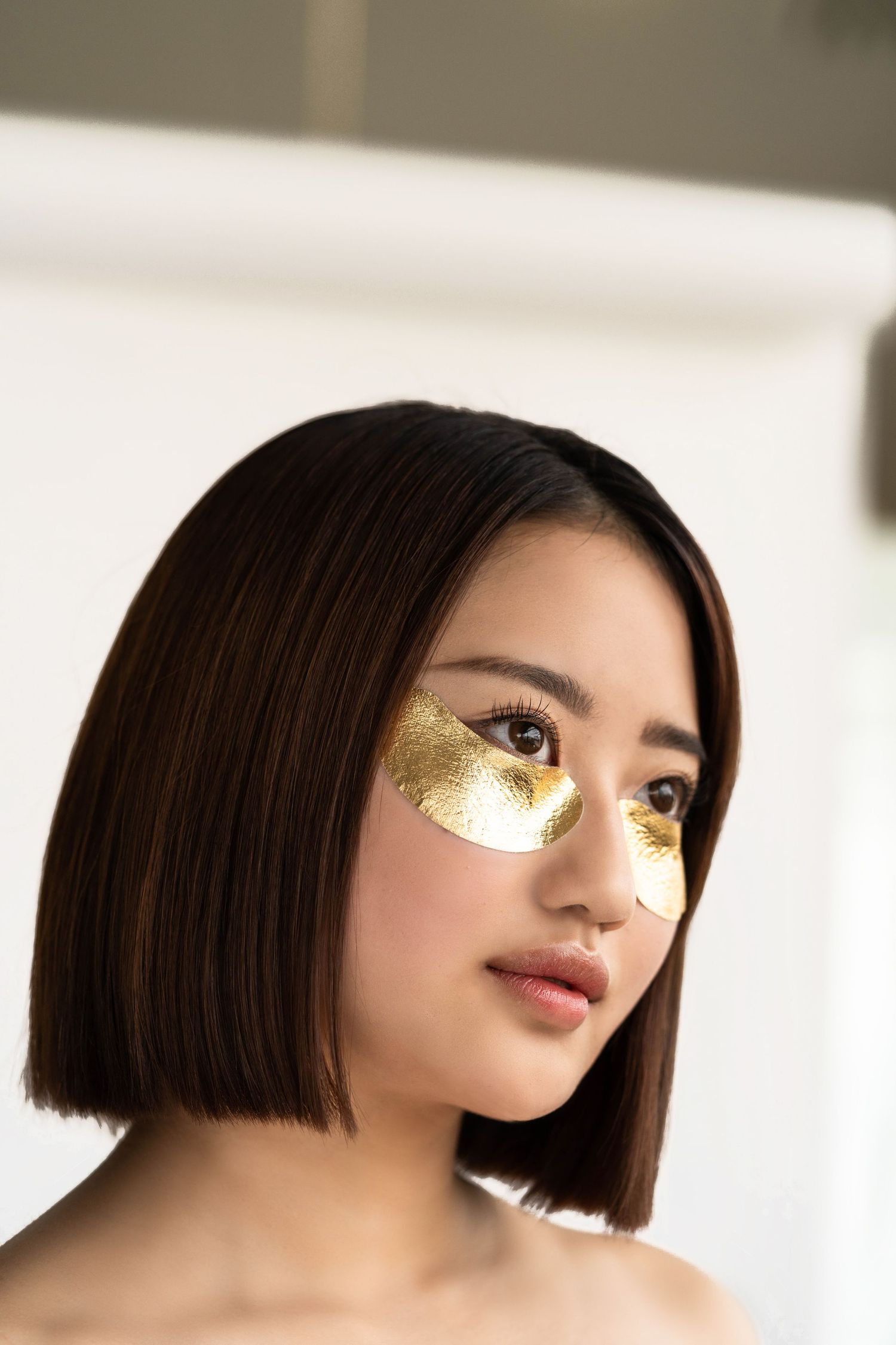 model fotografie voor een beauty merk, model heeft goudkleurige oog pads onder ogen en staat voor witte achtergrond.