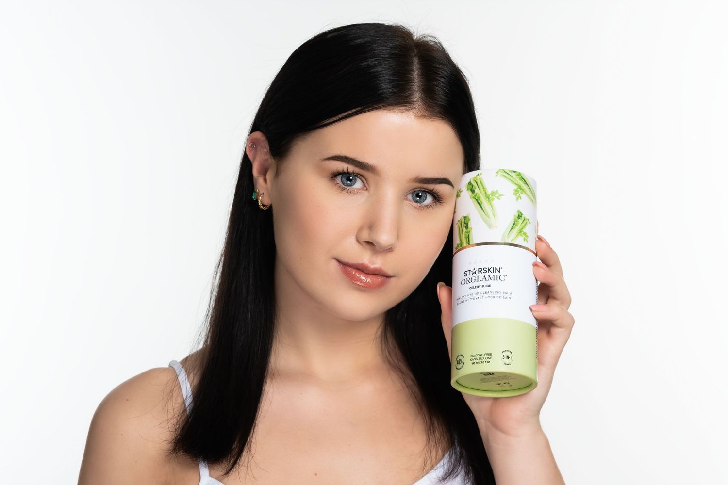 model met donker haar houdt verpakking van beauty product tegen gezicht en kijkt in camera.  witte achtergrond in studio in Eindhoven