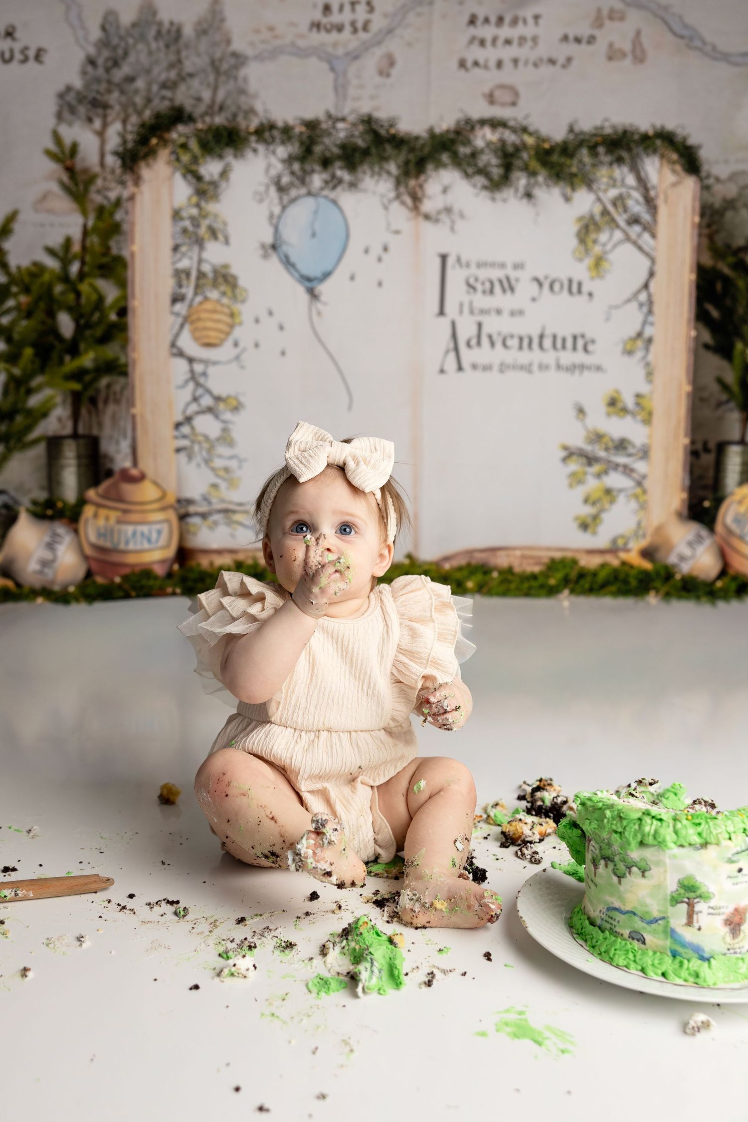 Baby girl smashing green cake at Winnie the Pooh themed first birthday cake smash photo session.