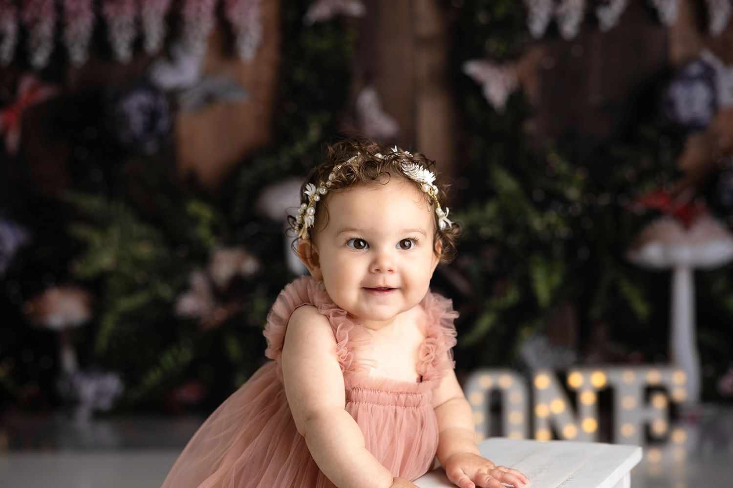 Smiling baby wearing floral crown and pink dress during studio photography session.