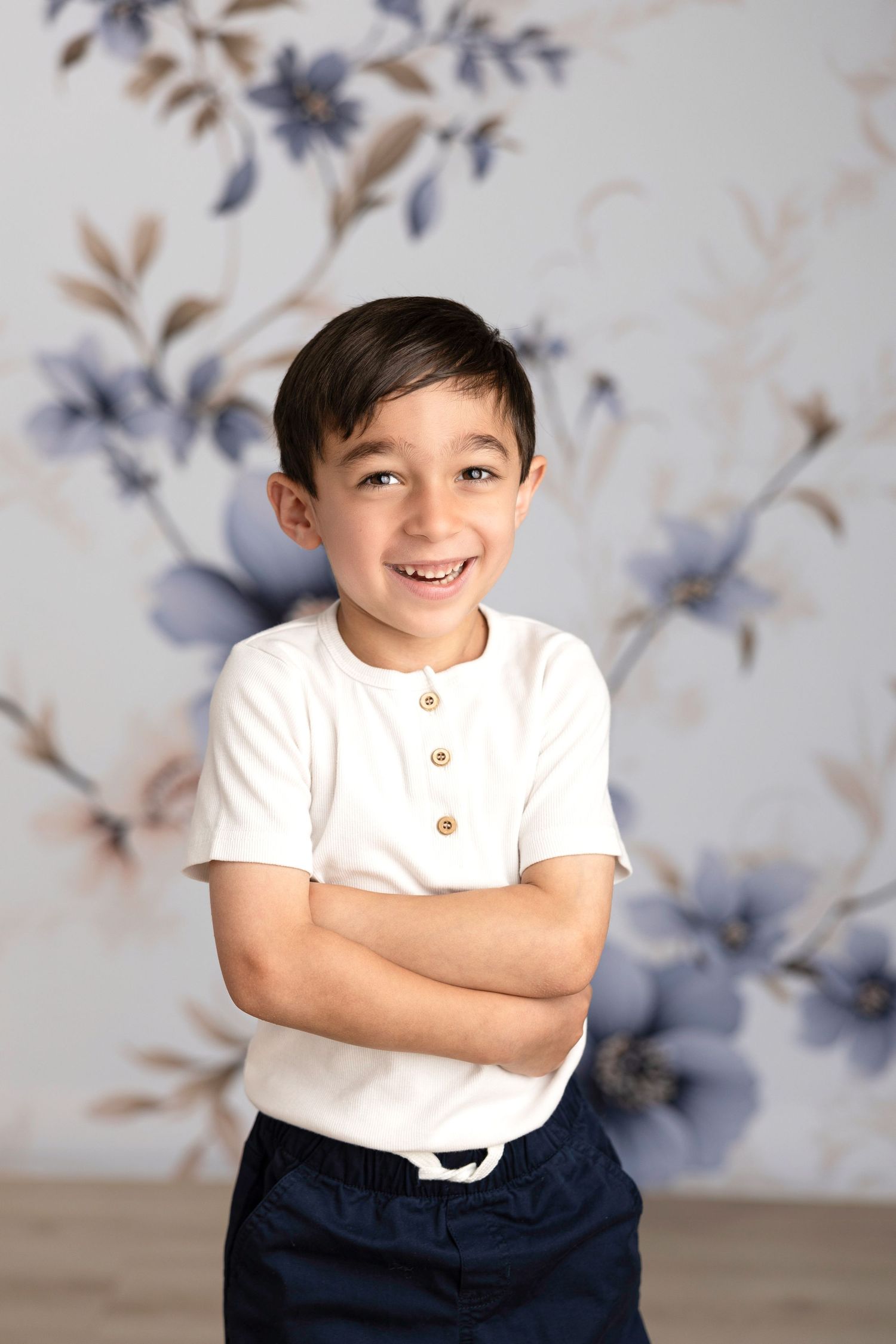 Cheerful poses of a child wearing a white shirt and navy pants against a floral background.