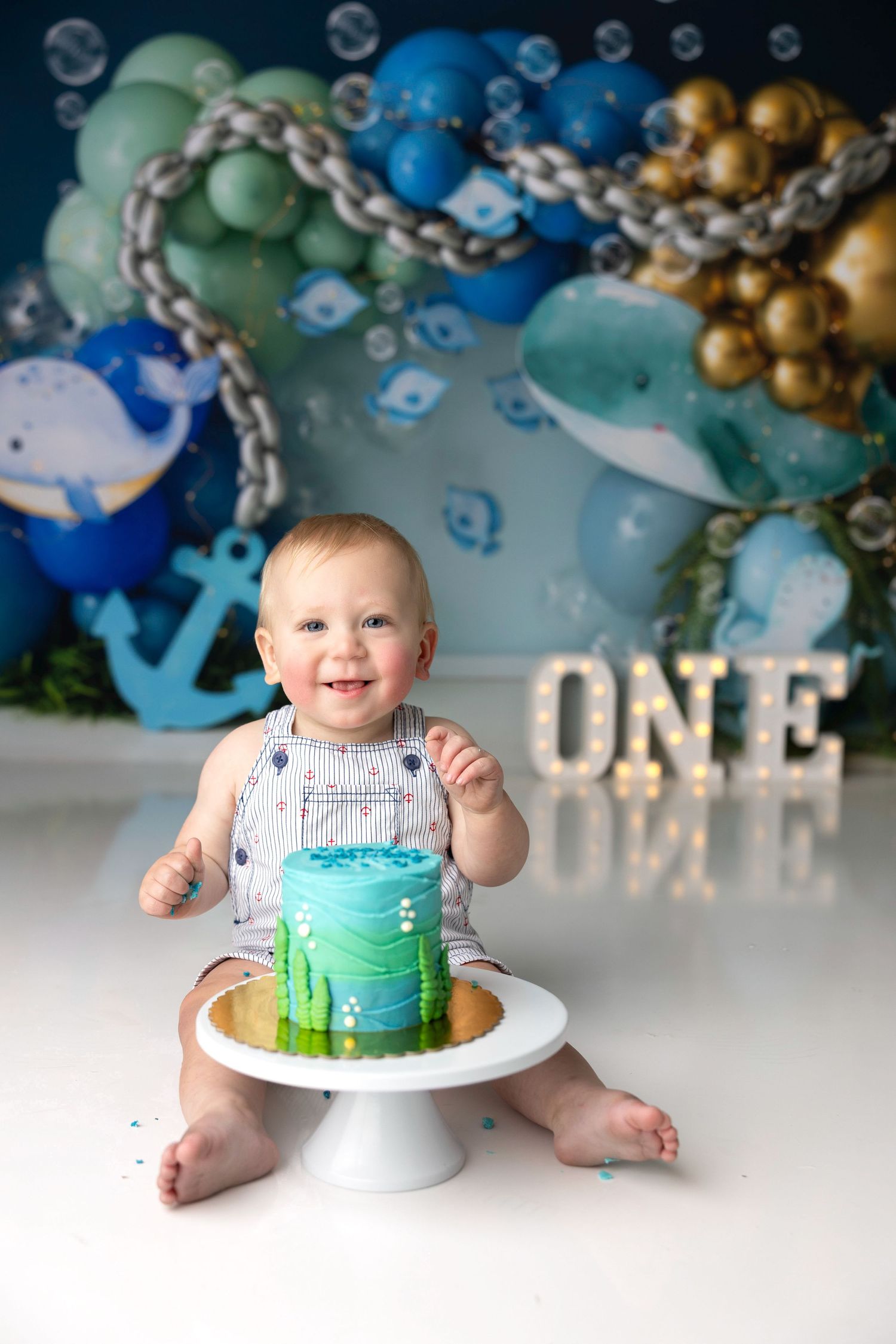 First birthday celebration with blue and gold balloon arch and smash cake setup.