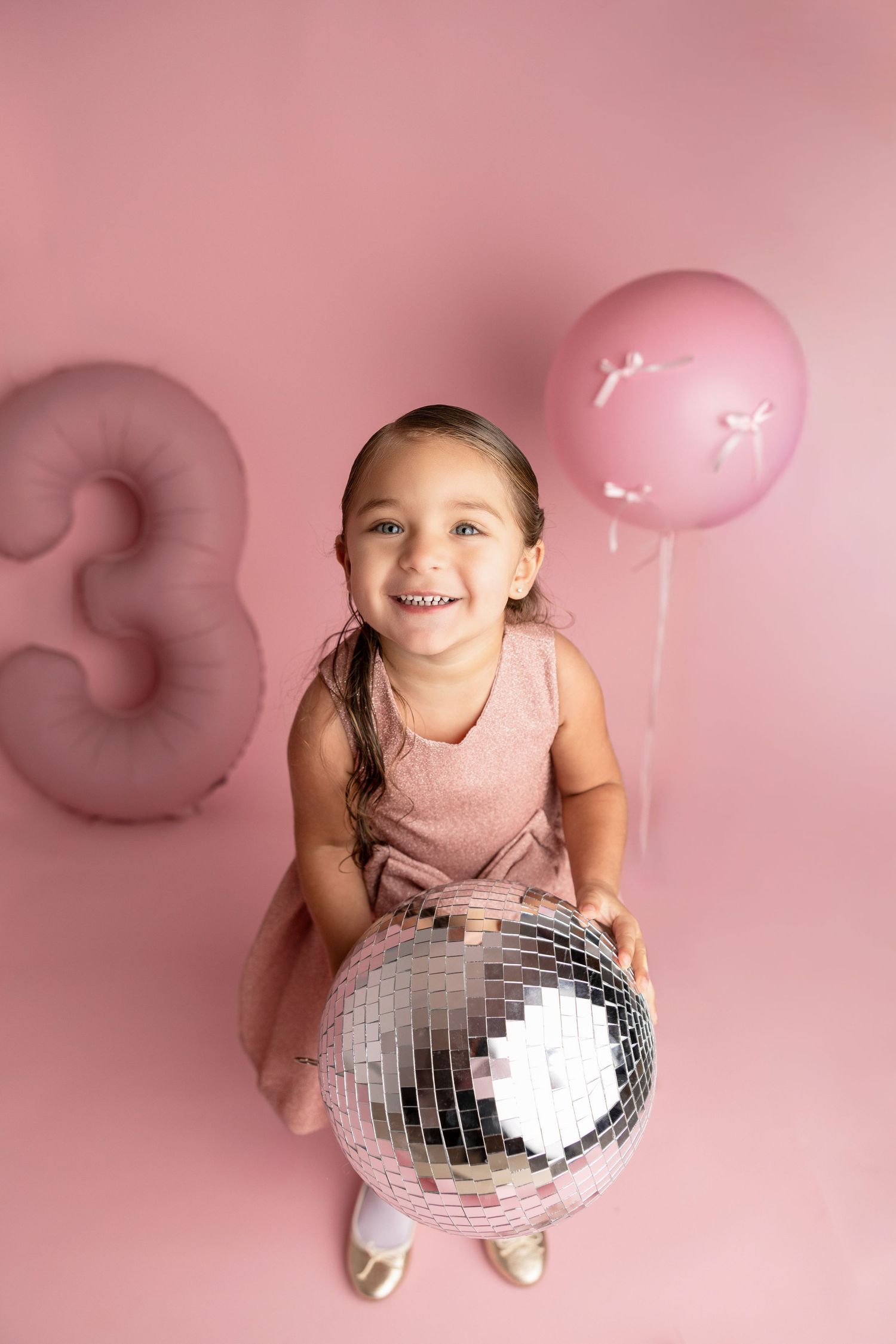 Playful pose with disco ball and pink balloon against pink background.
