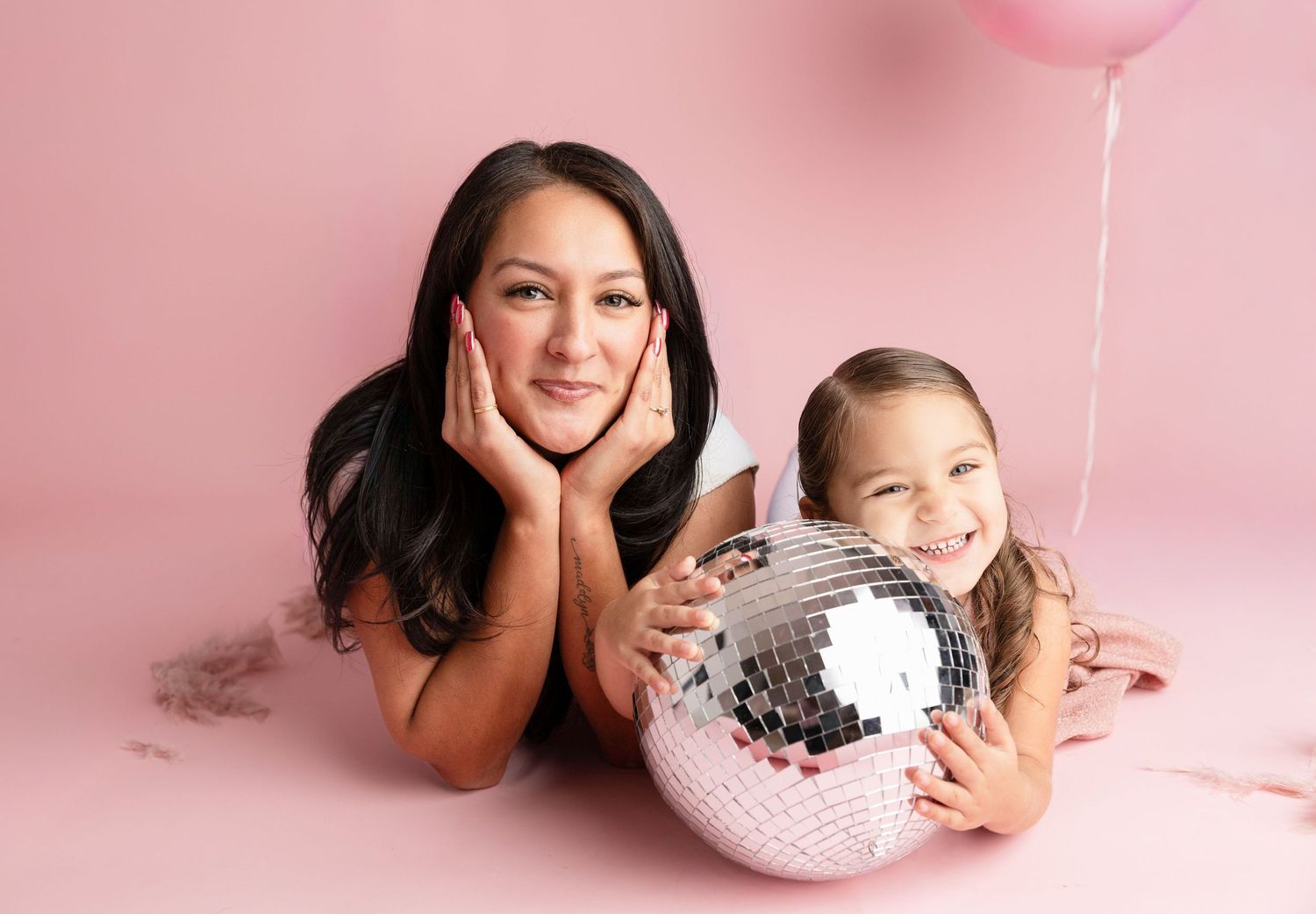 Studio portrait with disco ball and balloon against pink backdrop.
