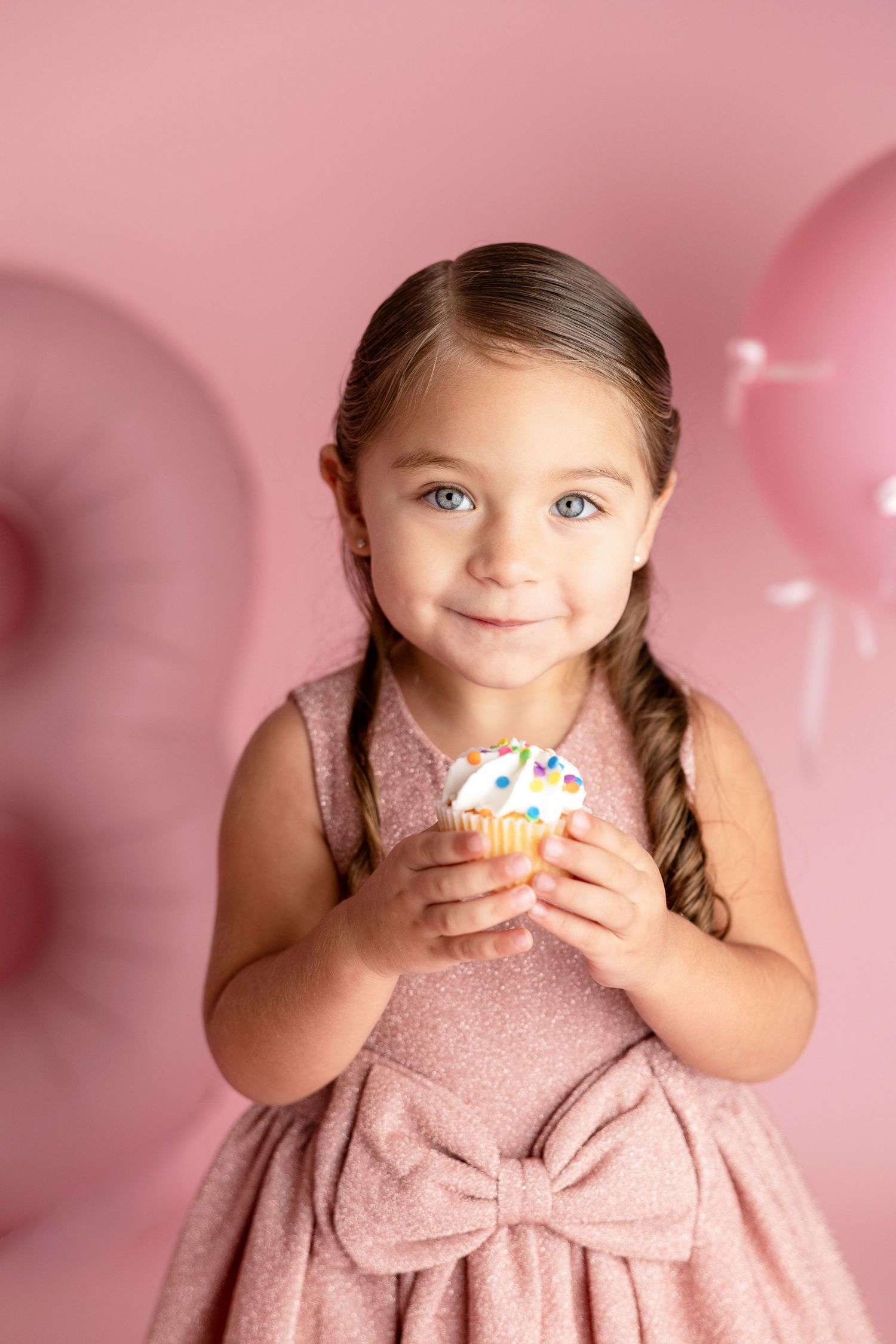 Sweet portrait holding cupcake in pink dress against pink background.