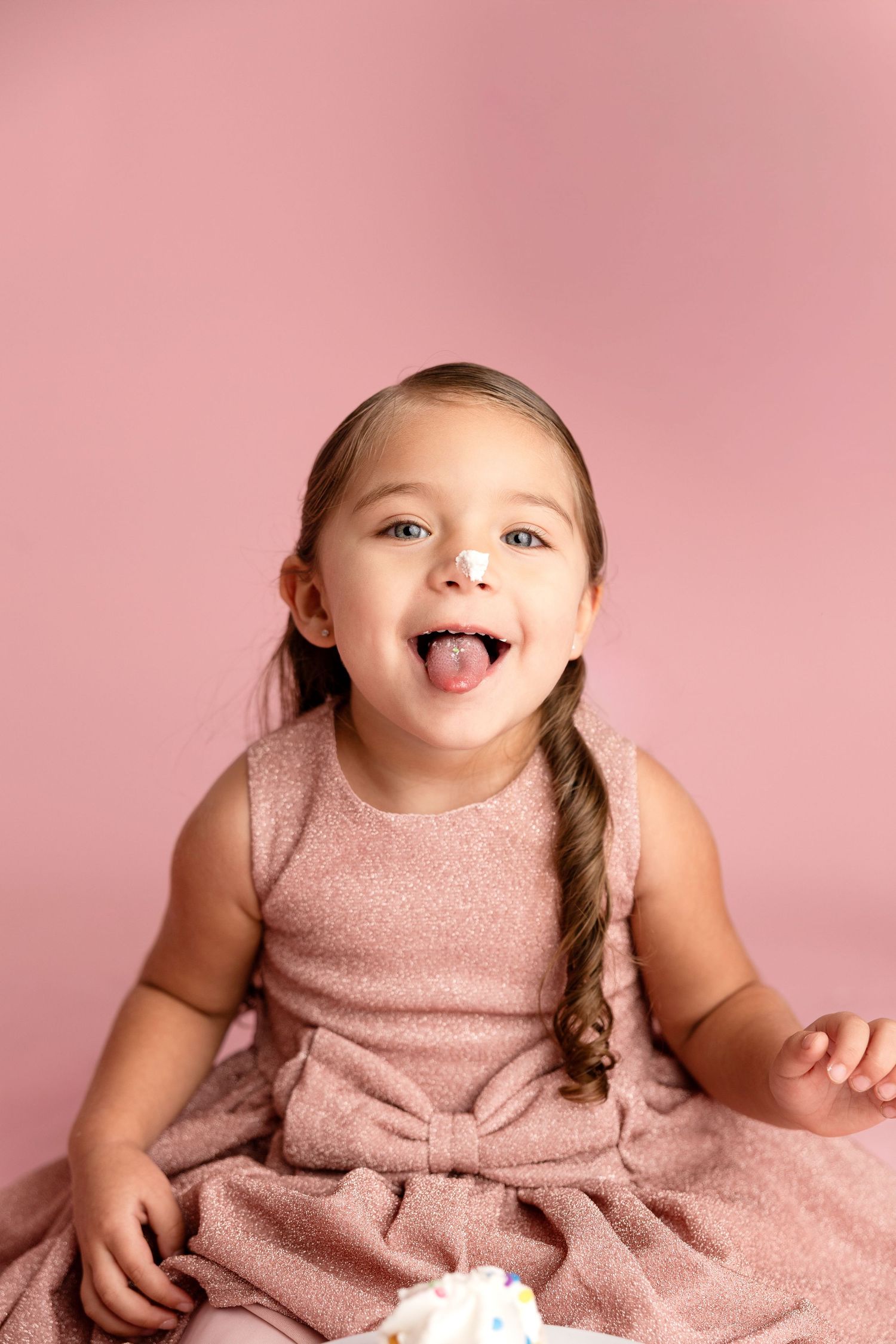 Playful expression in pink dress against solid pink background.