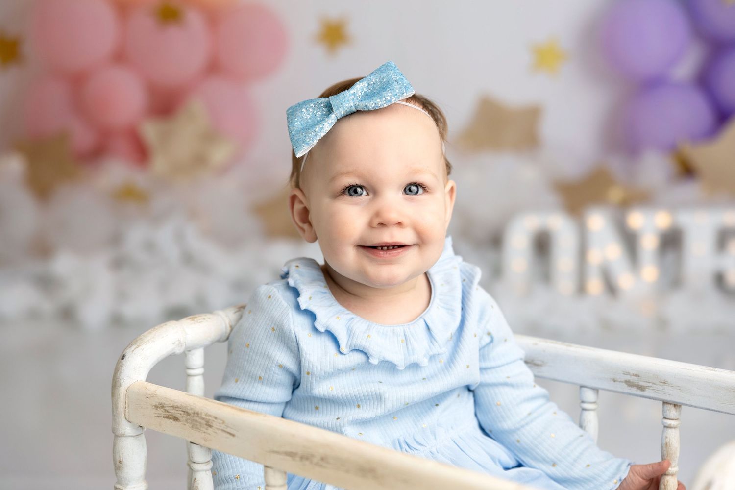 Baby portrait in blue dress and bow against pastel balloon backdrop.