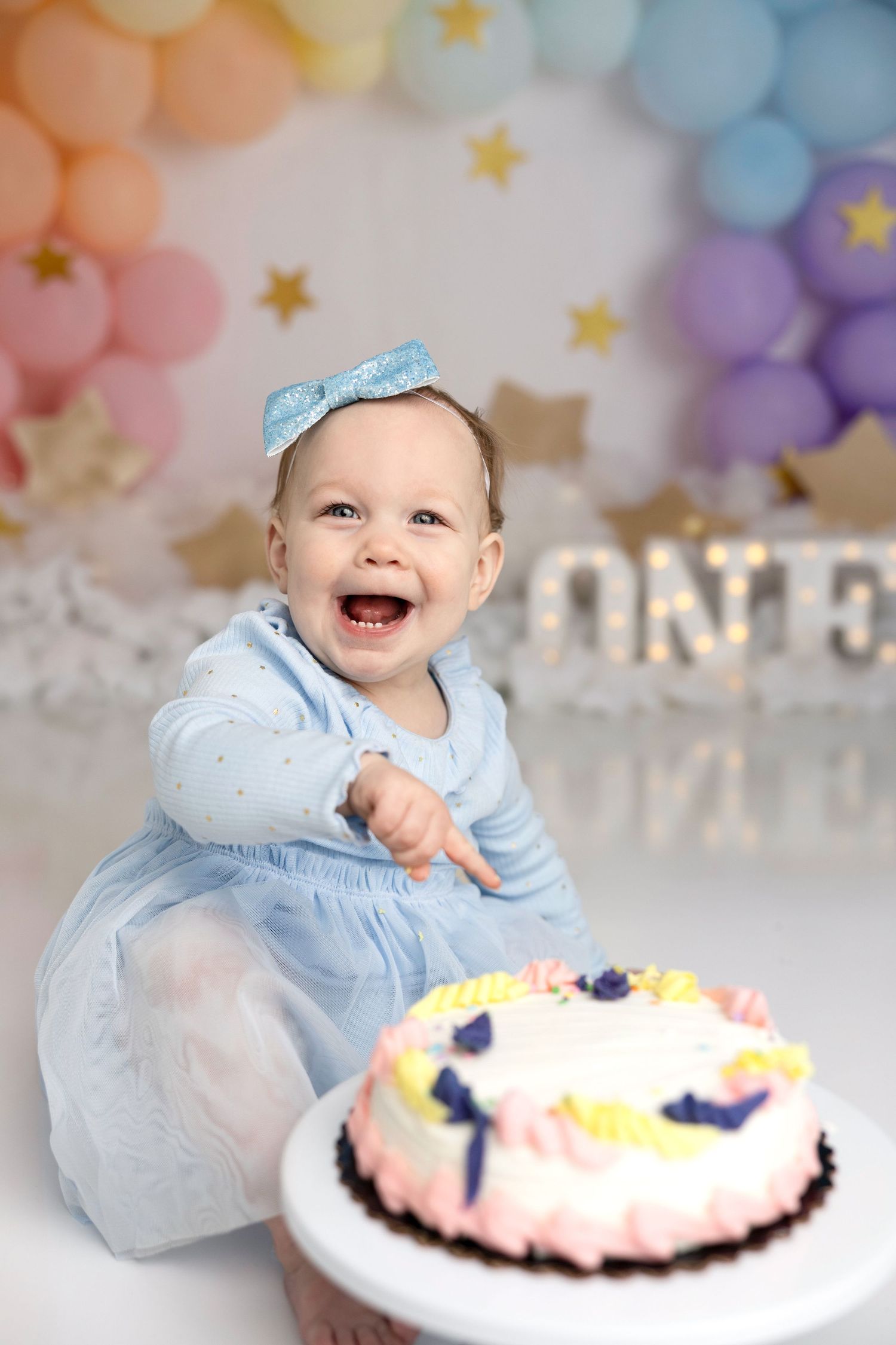 A first birthday celebration with a decorated cake and pastel balloon arch backdrop.