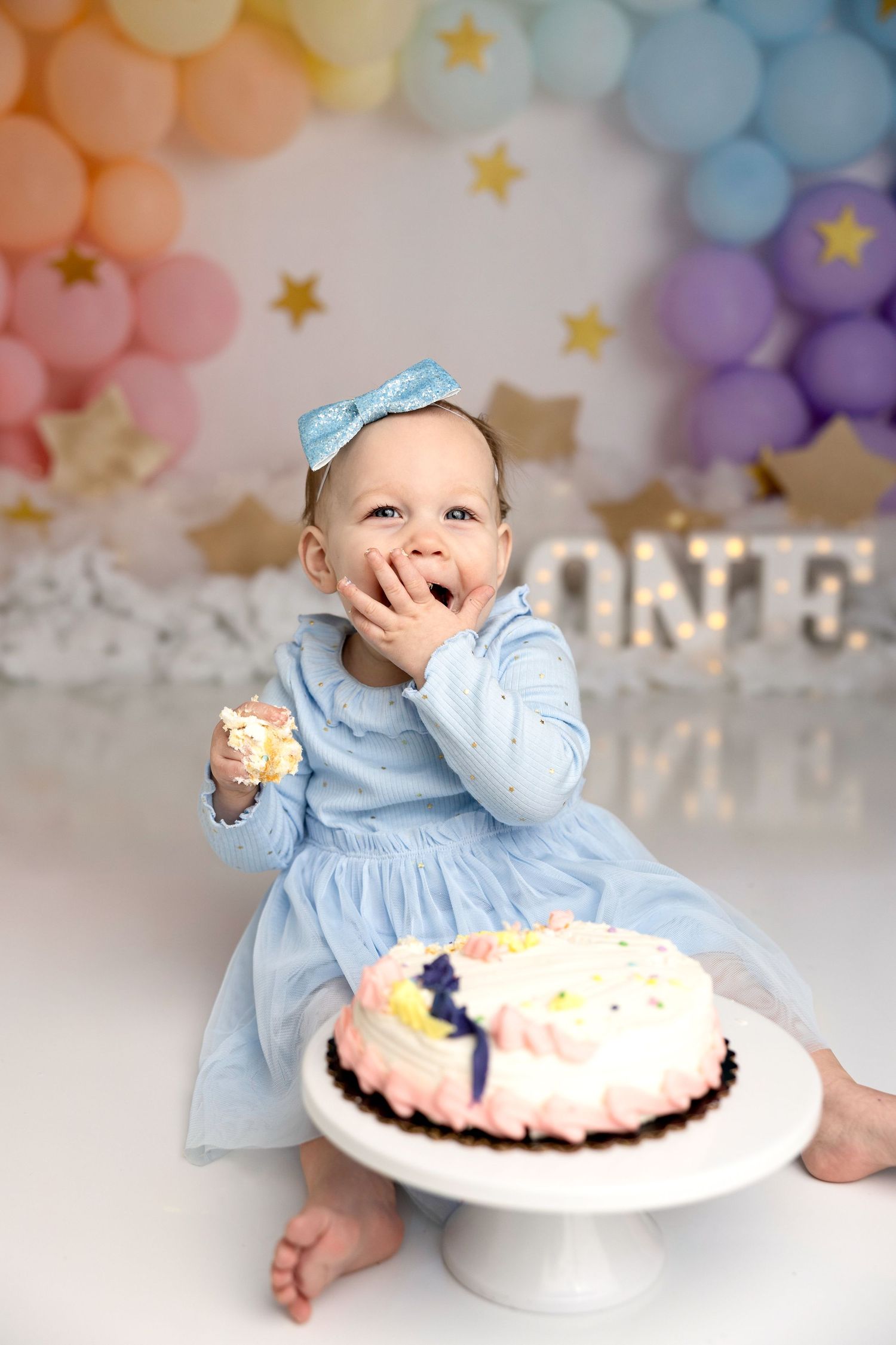 A joyful cake smash photo session with light blue dress and colorful balloon decorations.