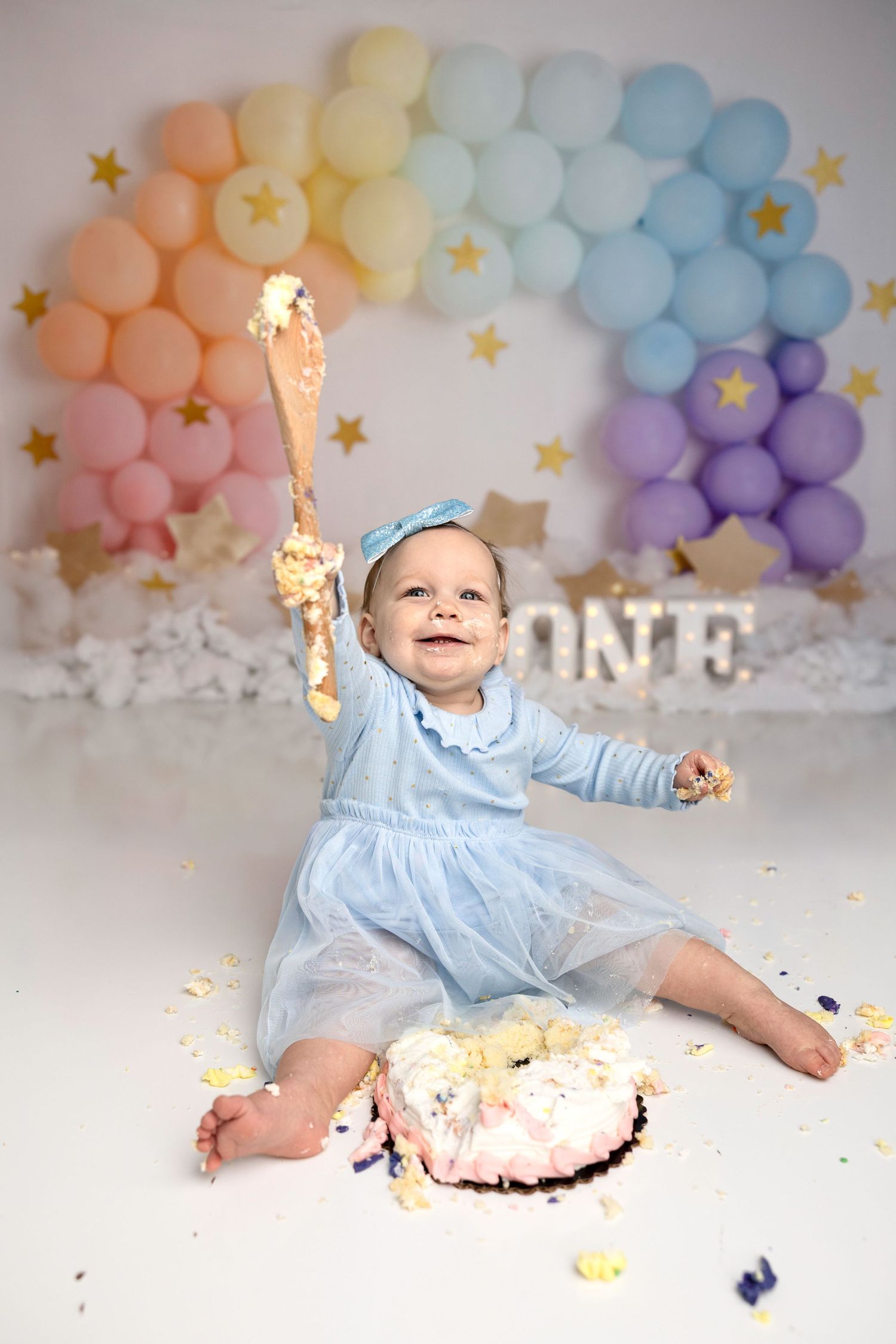 Cake smash photography session showing messy fun with pink frosting and pastel balloon backdrop.