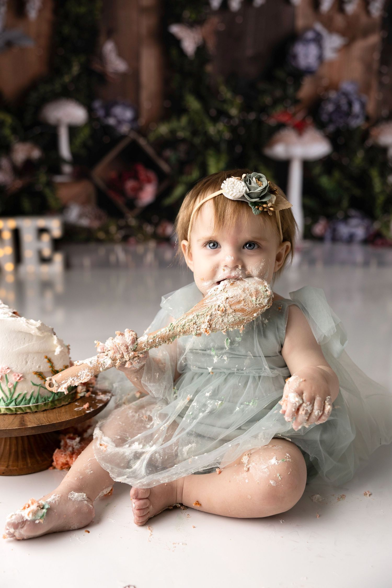 Messy cake smash photography session with baby in mint dress enjoying their birthday dessert.