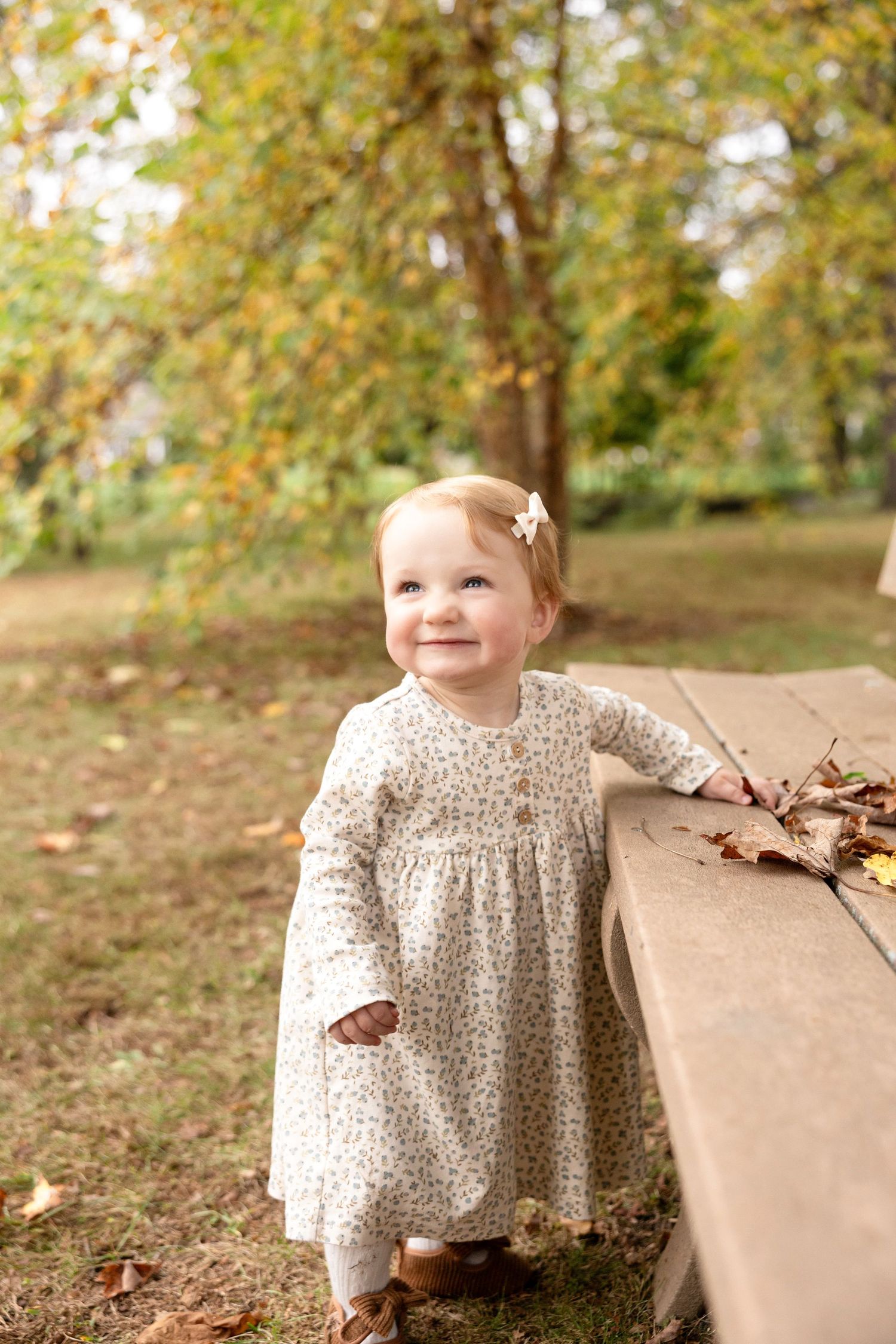 Child wearing floral dress playing with autumn leaves outdoors.
