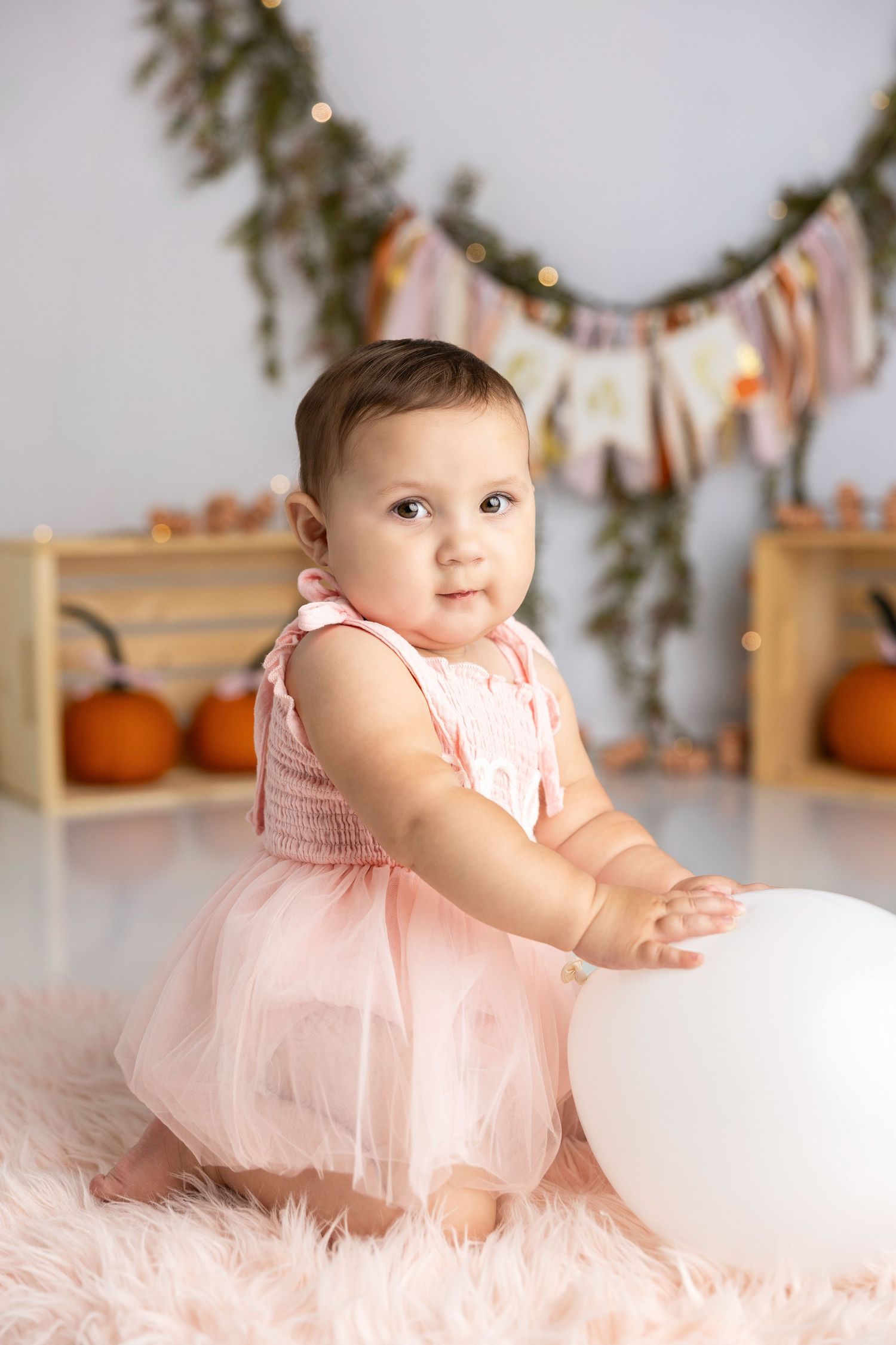 Baby in pink tulle dress at autumn themed photoshoot with pumpkins and garland decorations.