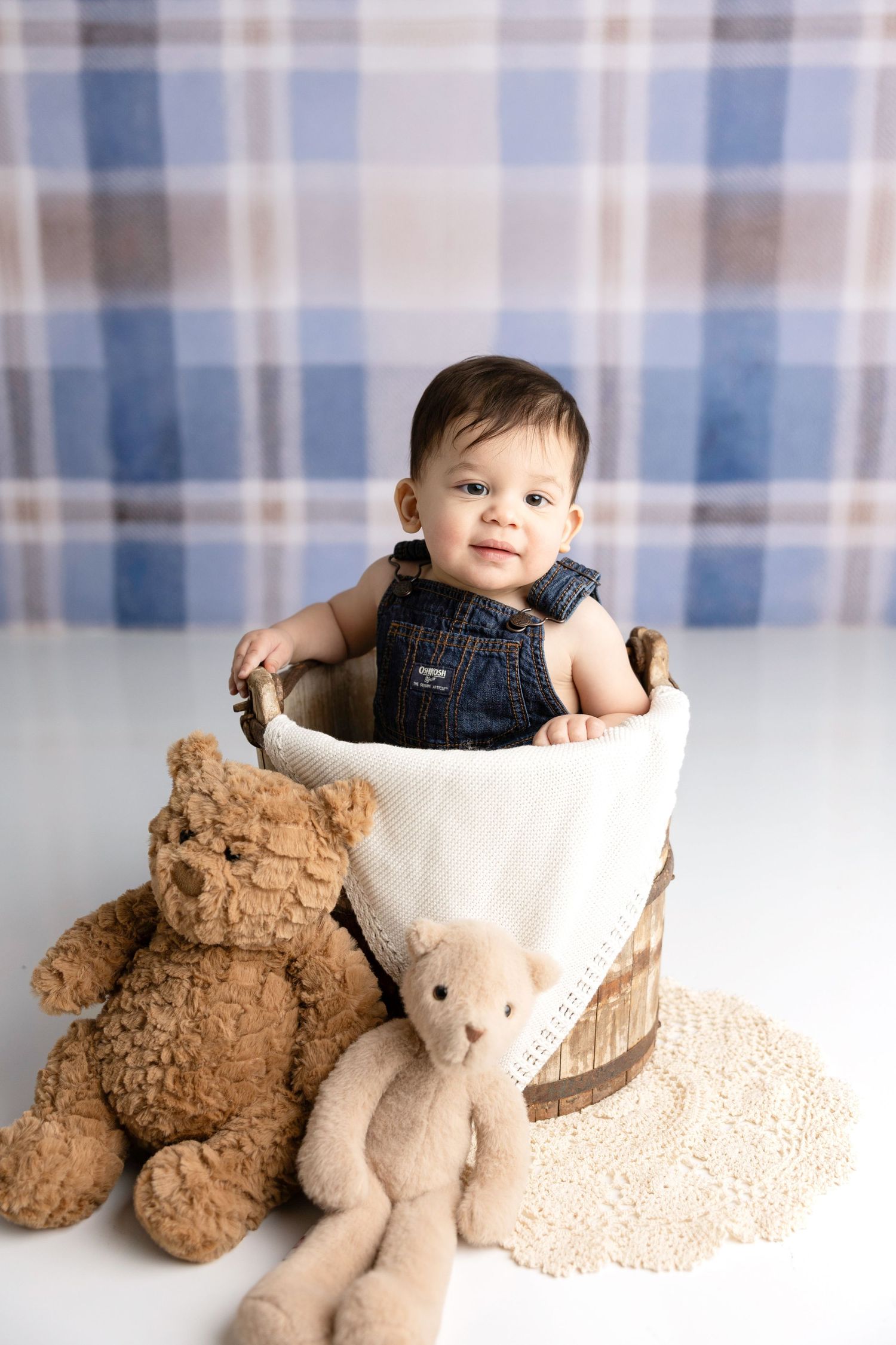 Baby nestled in white blanket with teddy bears on soft textured background.