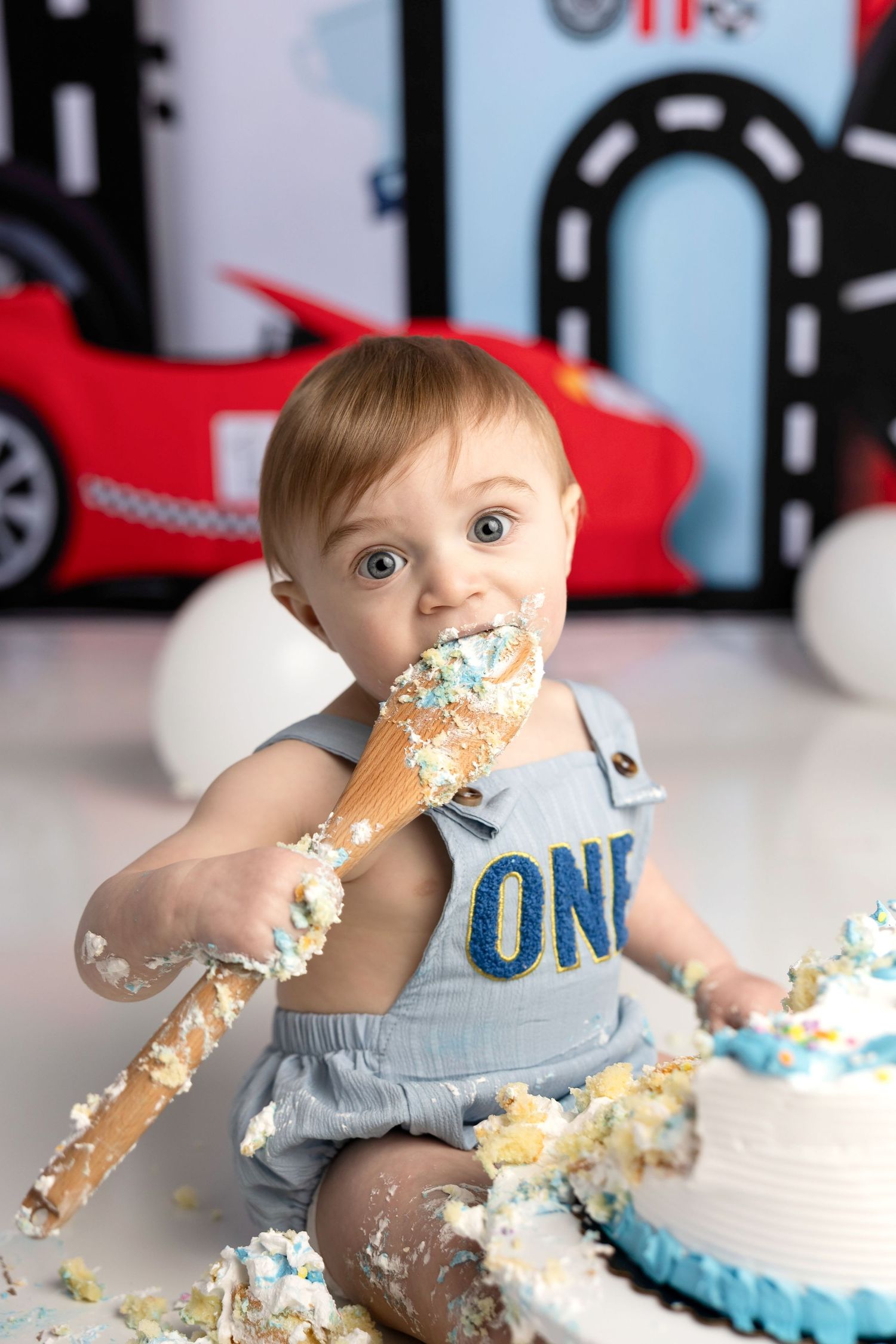 Baby in light blue outfit enjoying first birthday cake smash session with frosting and cake all over their face and hands.
