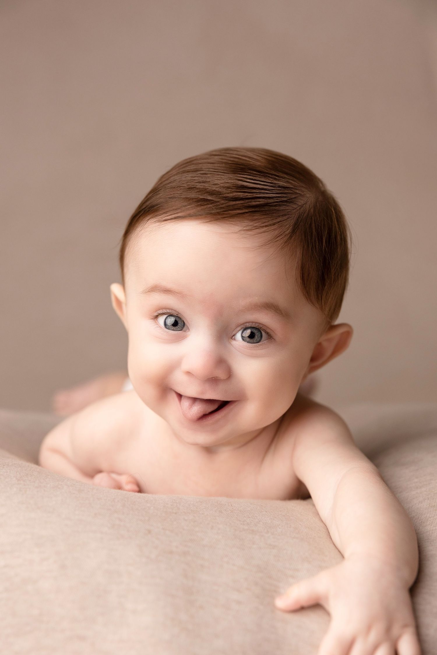 Smiling baby lying on beige blanket showing playful expression.