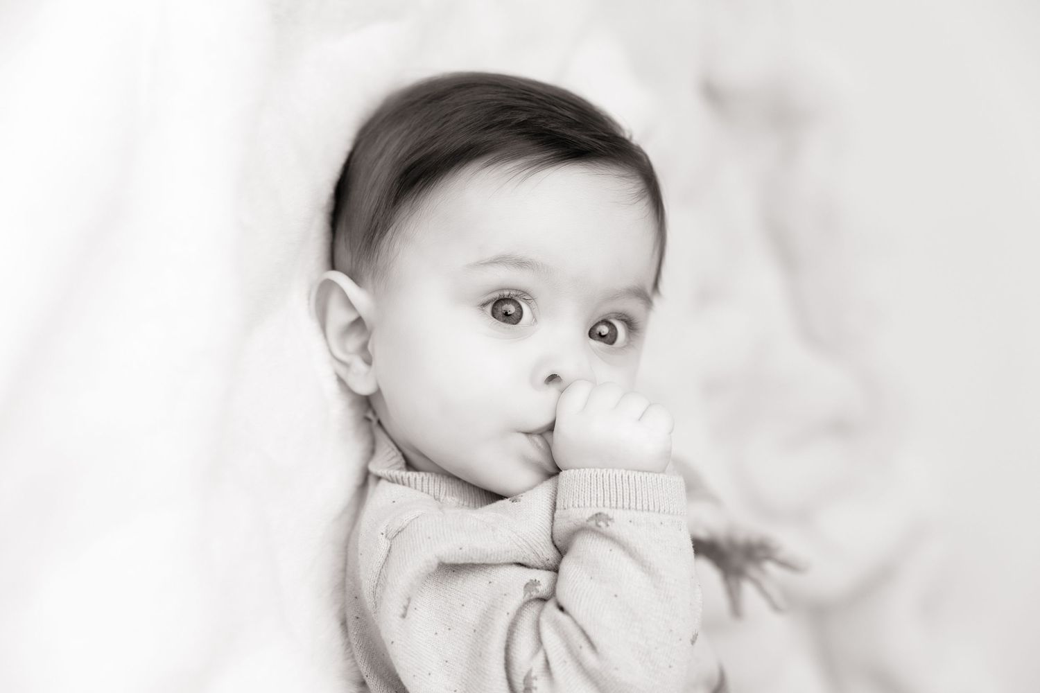 Black and white portrait of baby with finger near mouth.