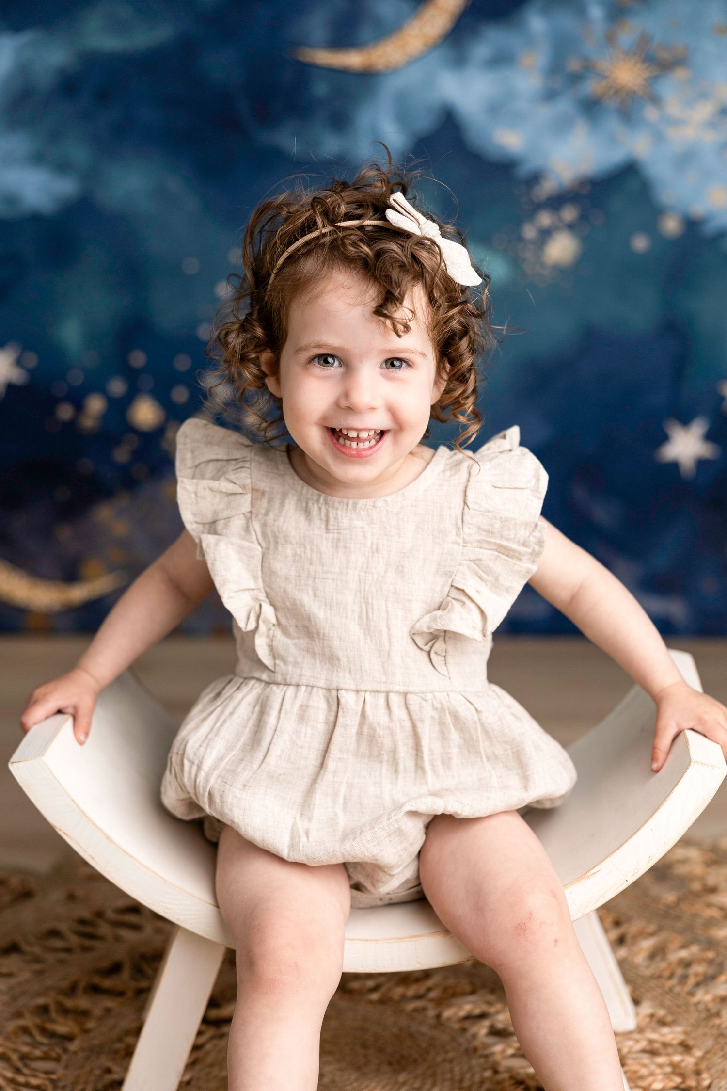Vintage-style portrait session with white romper against starry blue backdrop.