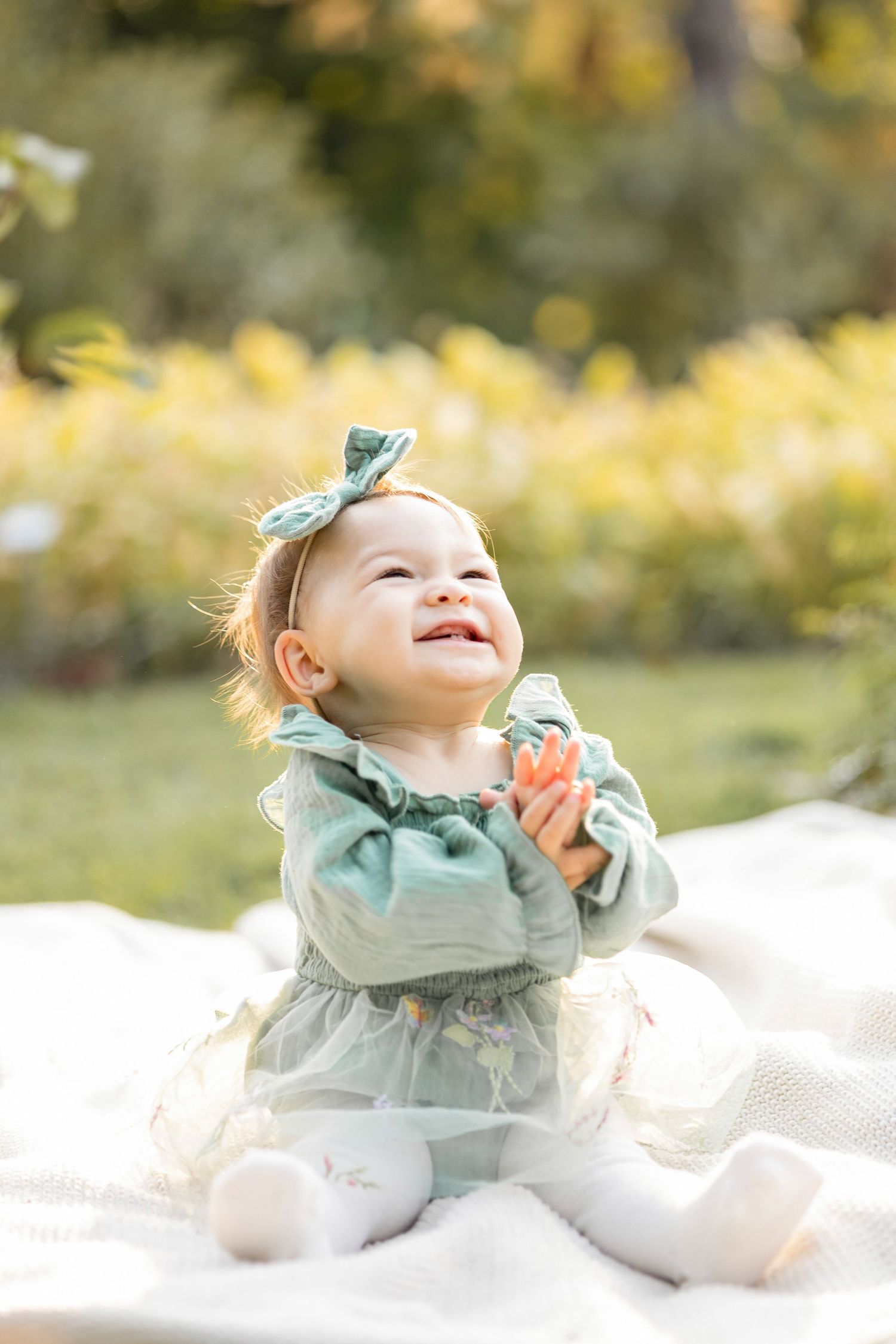 A baby in mint green outfit plays on white blanket during outdoor autumn photo session.