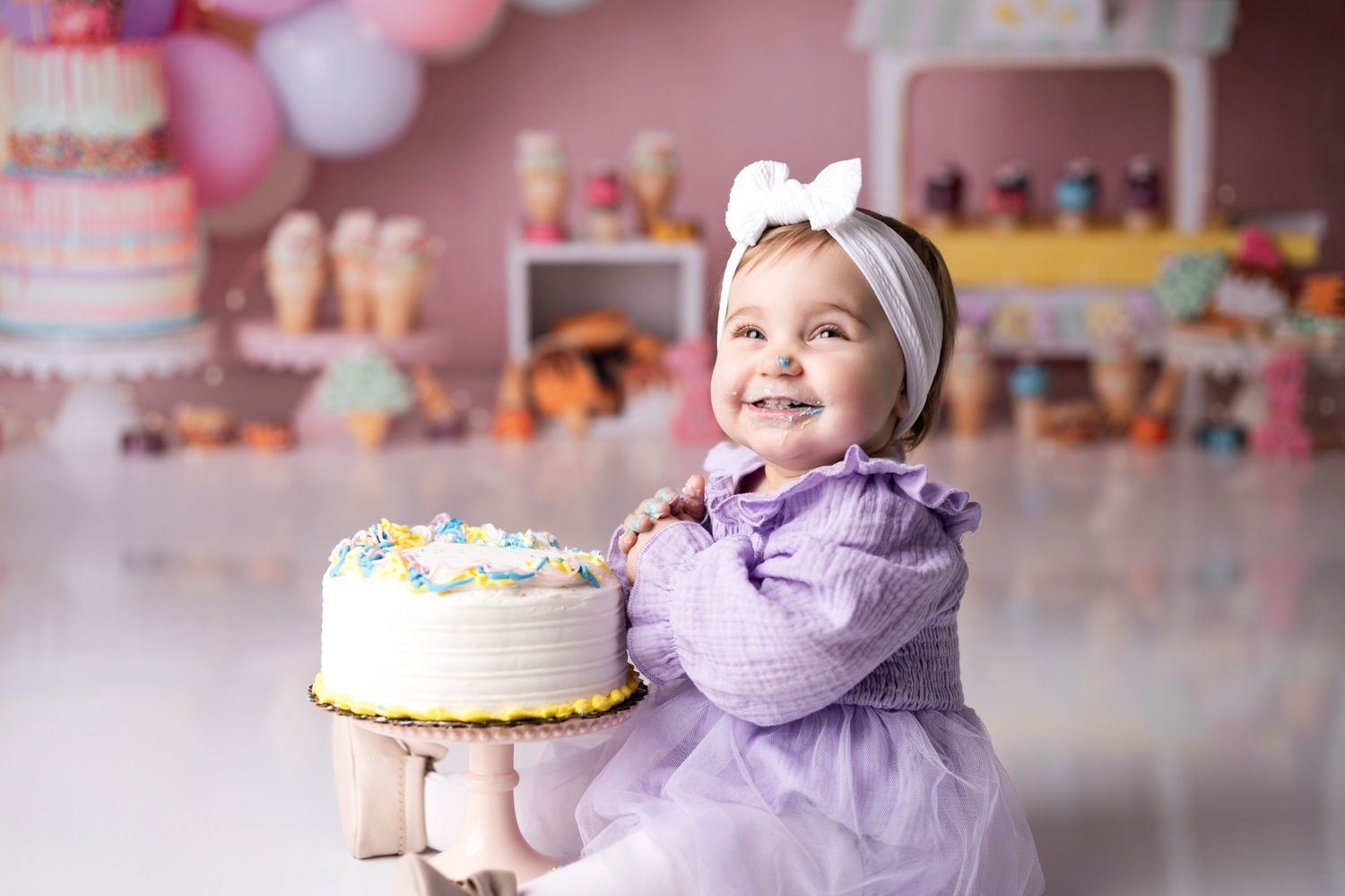 Festive first birthday scene with pink balloons, cake and party decorations.