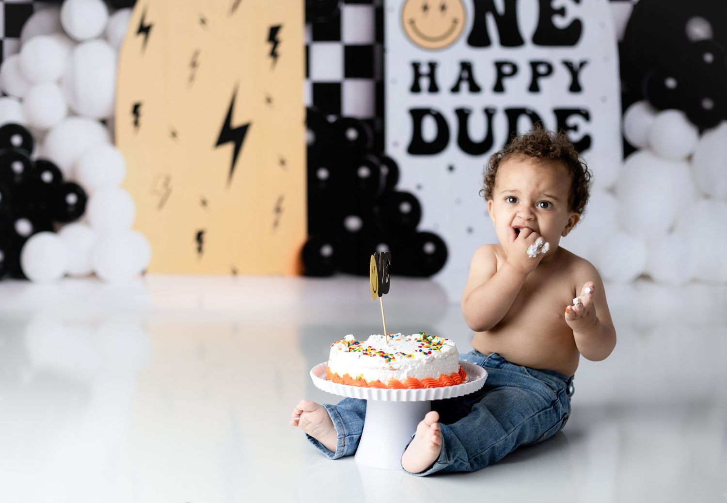 Cake smash photo session with lightning bolt backdrop and white balloons.