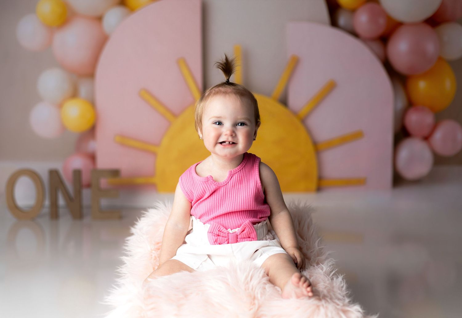 First birthday photo setup with pink and gold balloons and a sun backdrop for a celebration.