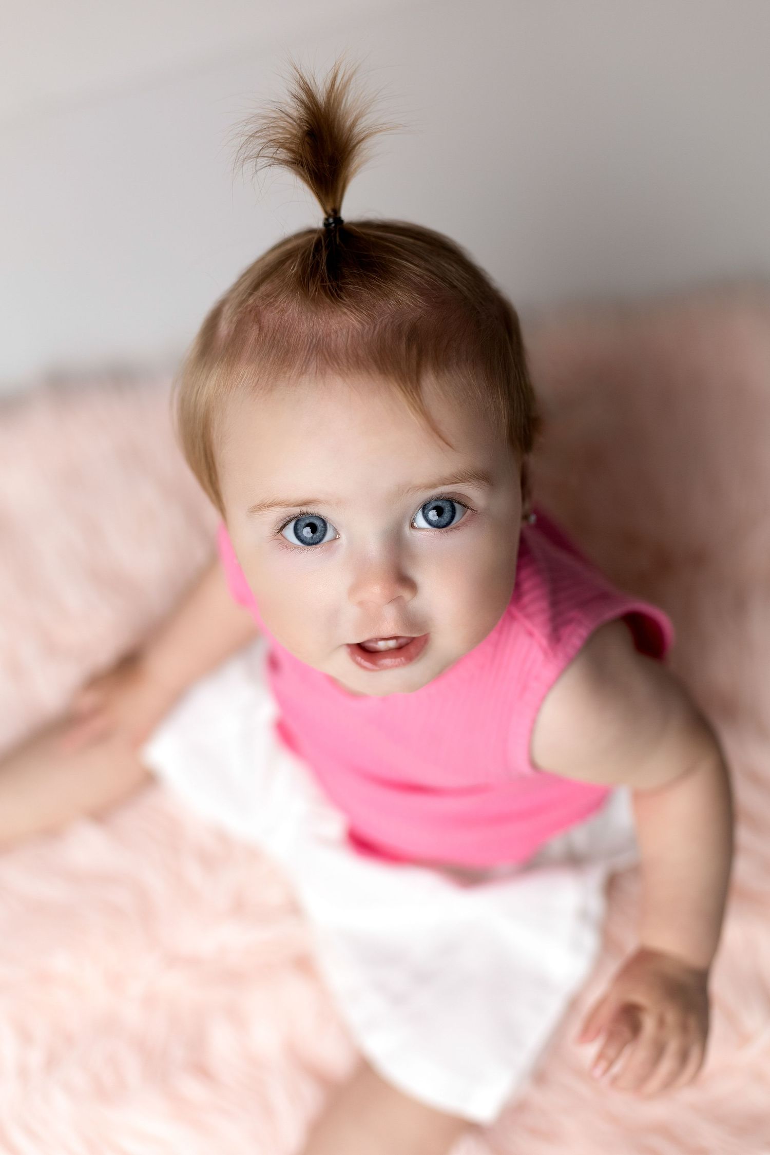 Baby in pink top on blush background with unique hairstyle.