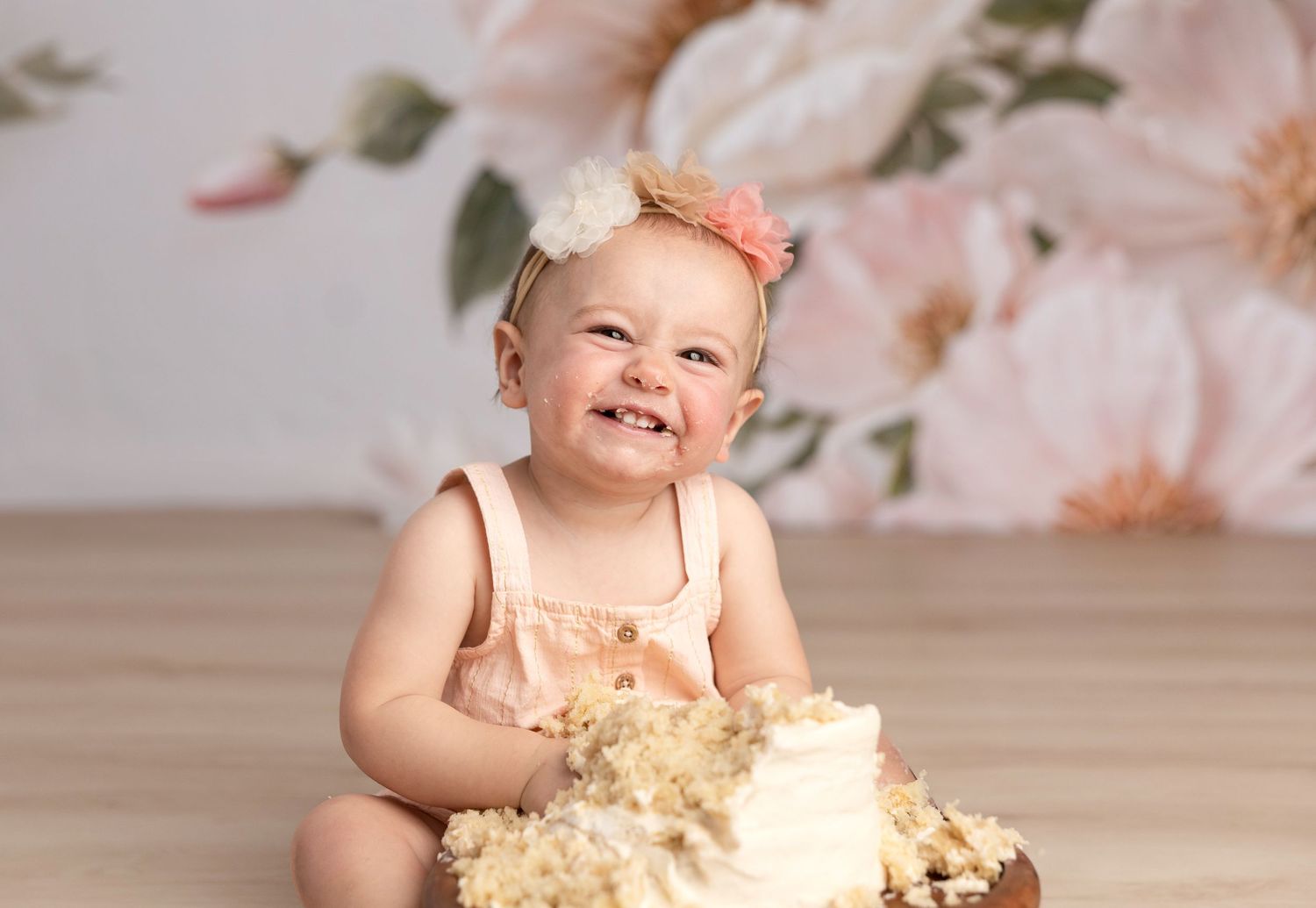 First birthday cake smash photo with pink floral backdrop and messy frosting.