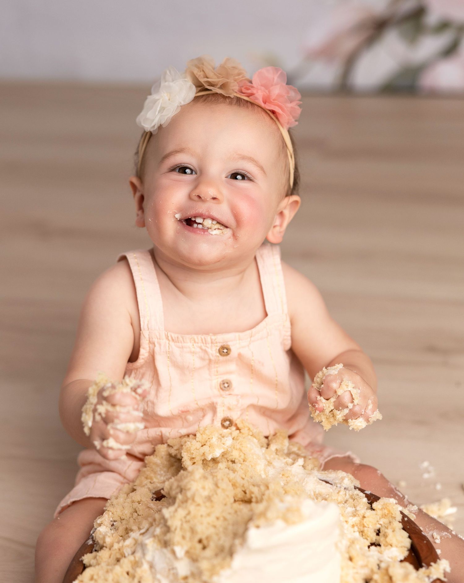 Happy baby in peach dress enjoying cake smash photo session with scattered crumbs.