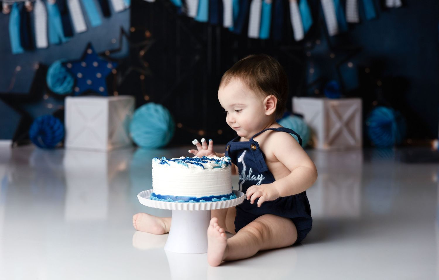 Baby cake smash photo session with blue decorations and white cake.