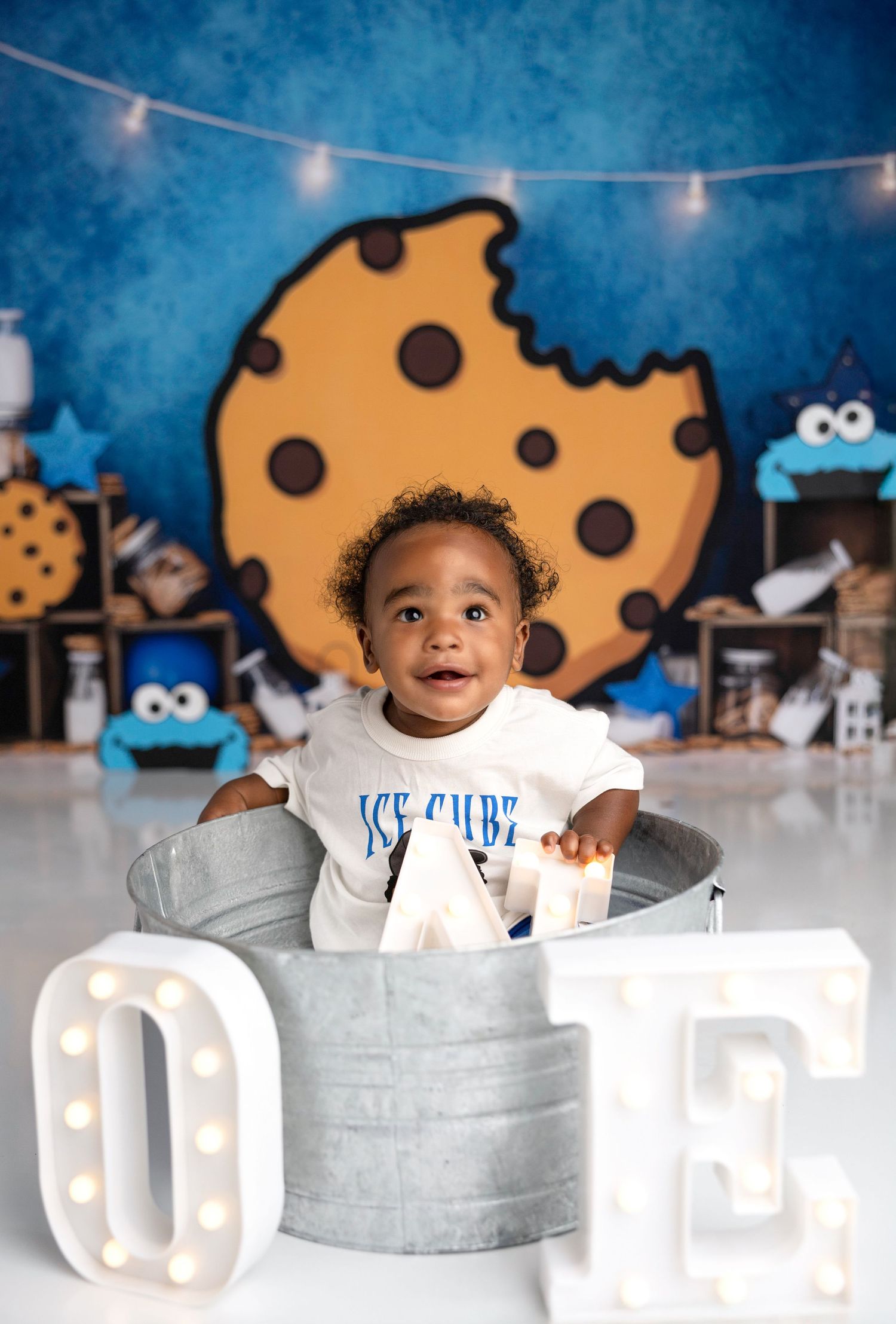 Baby sitting in white ONE letter display against blue background with cookie decorations.
