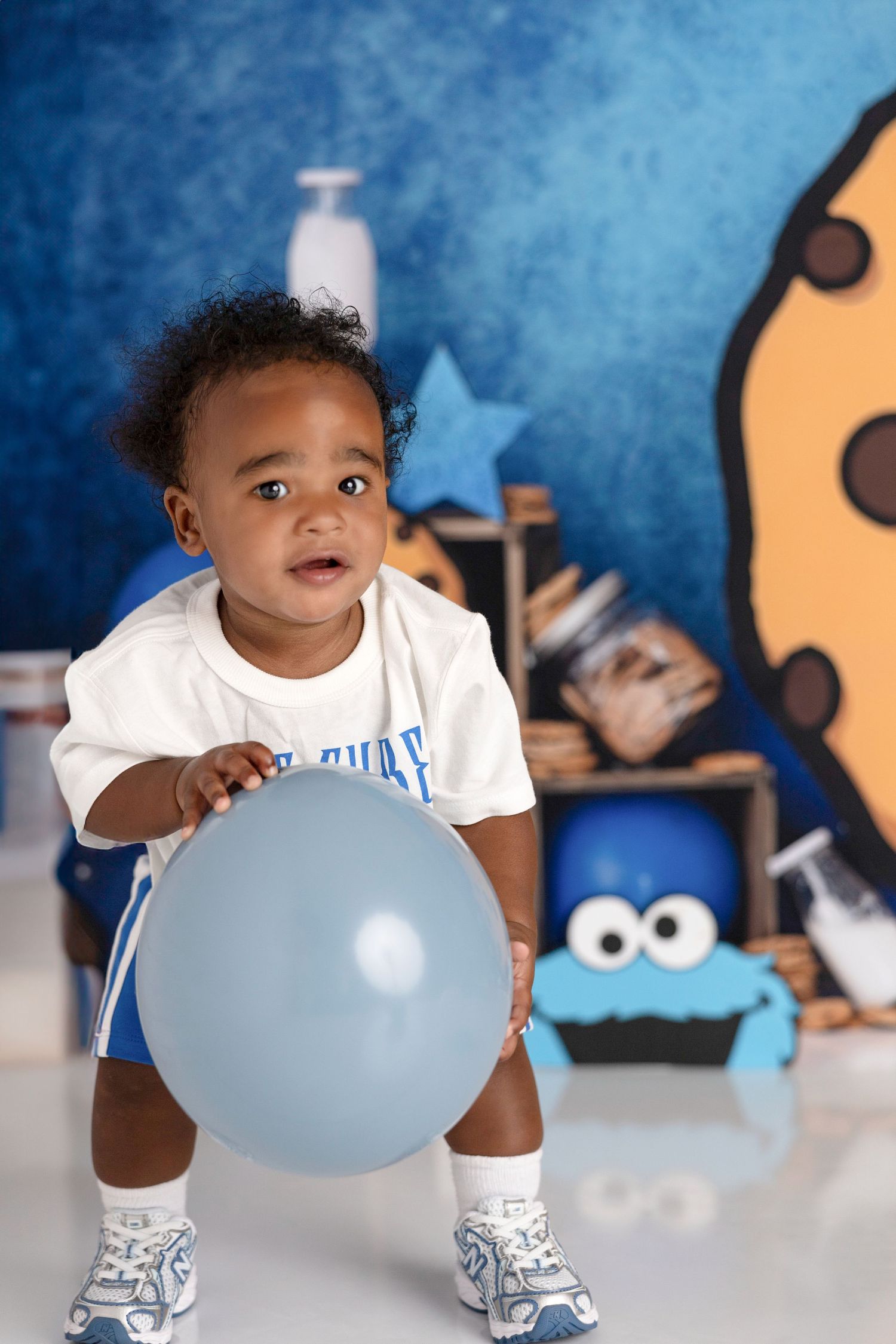 Baby playing with blue balloon against blue background with cookie decorations.