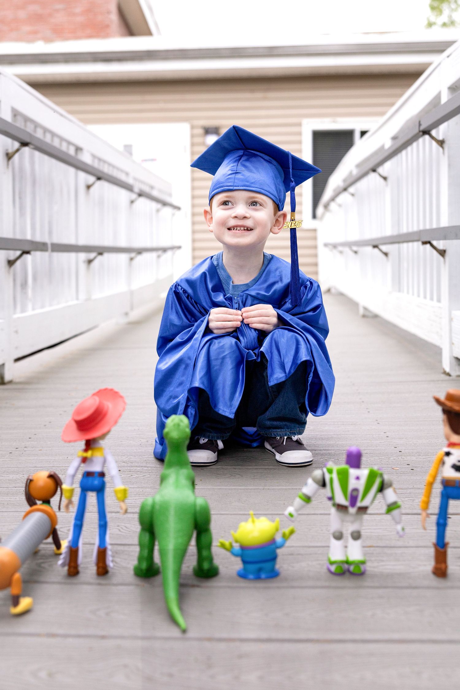 Small figure in blue graduation cap and gown posing with colorful toy figures on white steps.