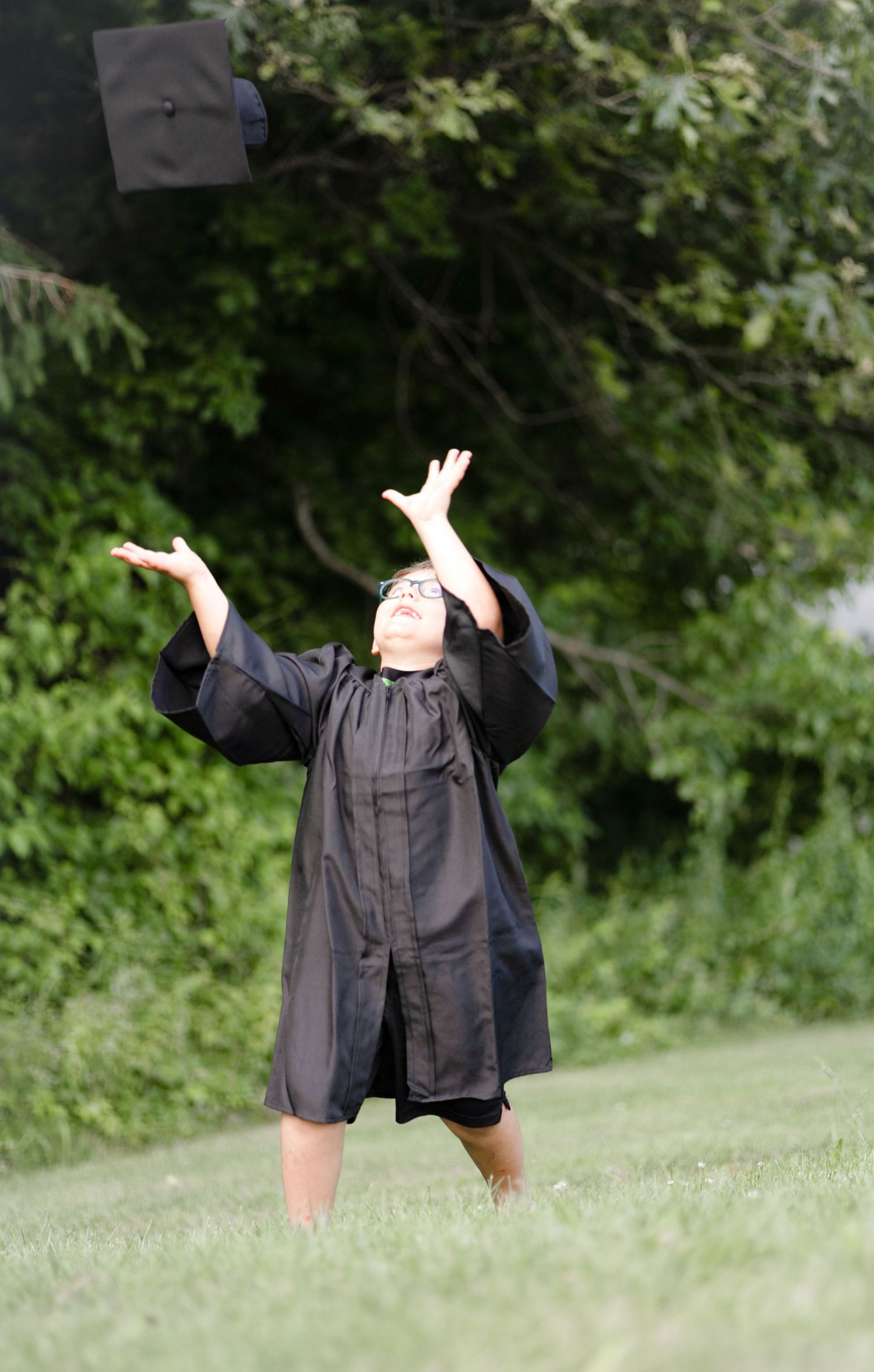 Graduate in black cap and gown tossing mortarboard in celebration outdoors.
