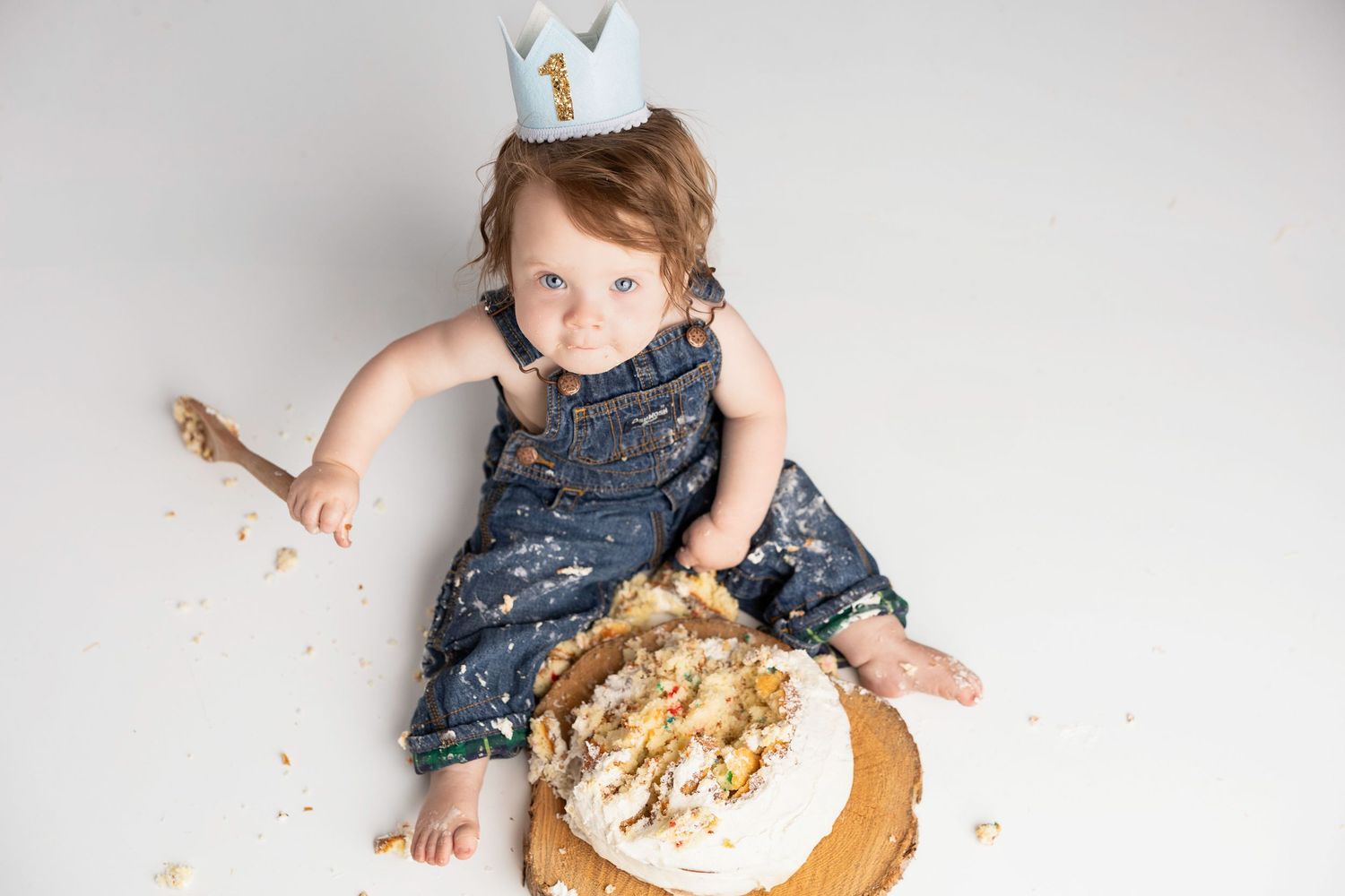 Baby in denim overalls playing with cake during smash session.