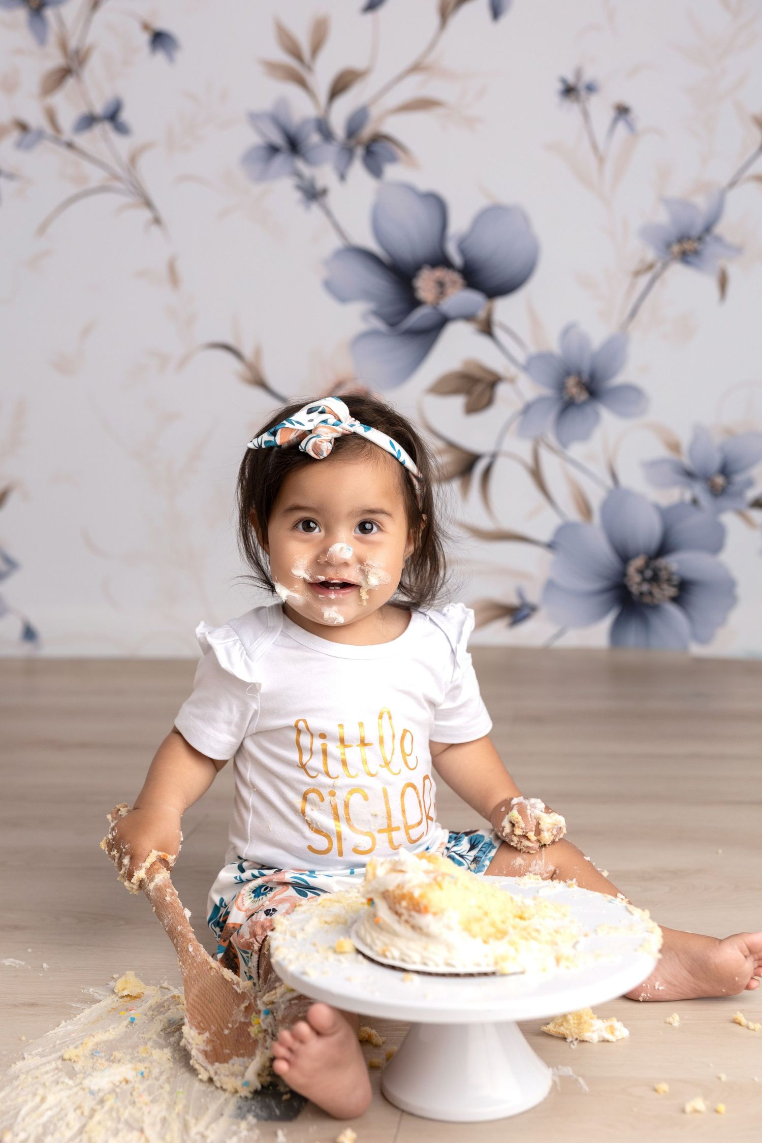 Cake smash photography session with floral backdrop and white cake stand.