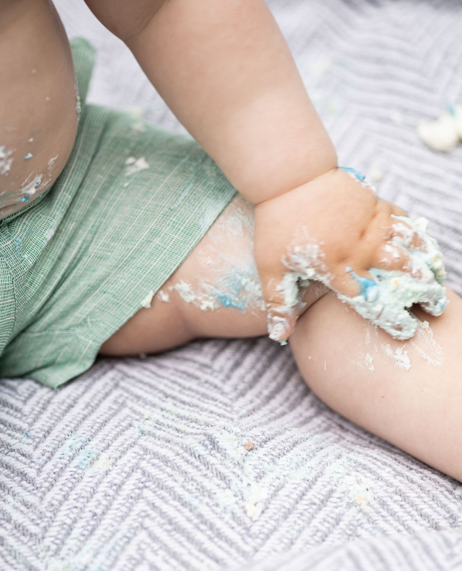 Close-up of tiny hands playing with cake frosting or icing on a textured gray surface.